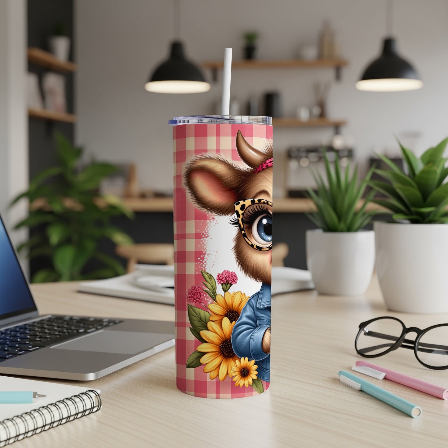 Cow tumbler with sunflowers and plaid pattern on desk with laptop and pens.