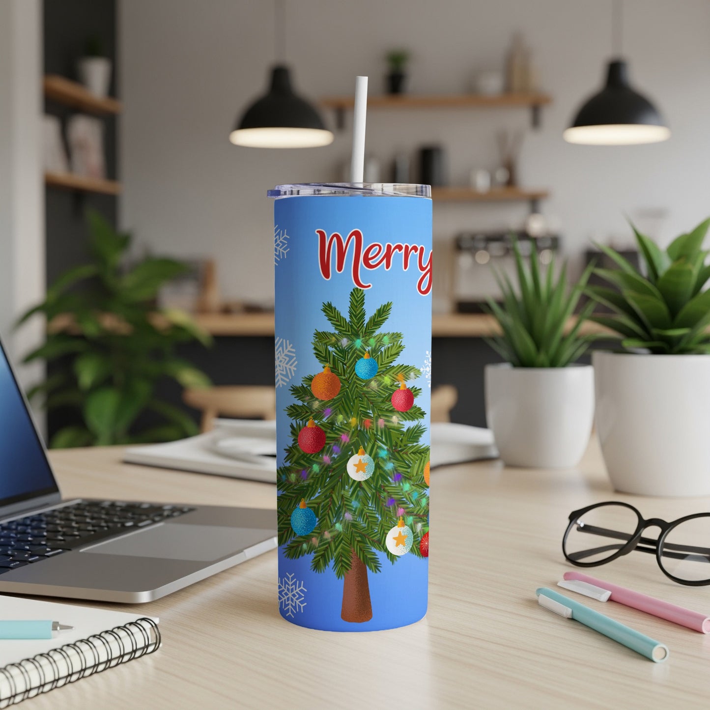 Blue tumbler with "Merry Christmas" and decorated tree on a desk.