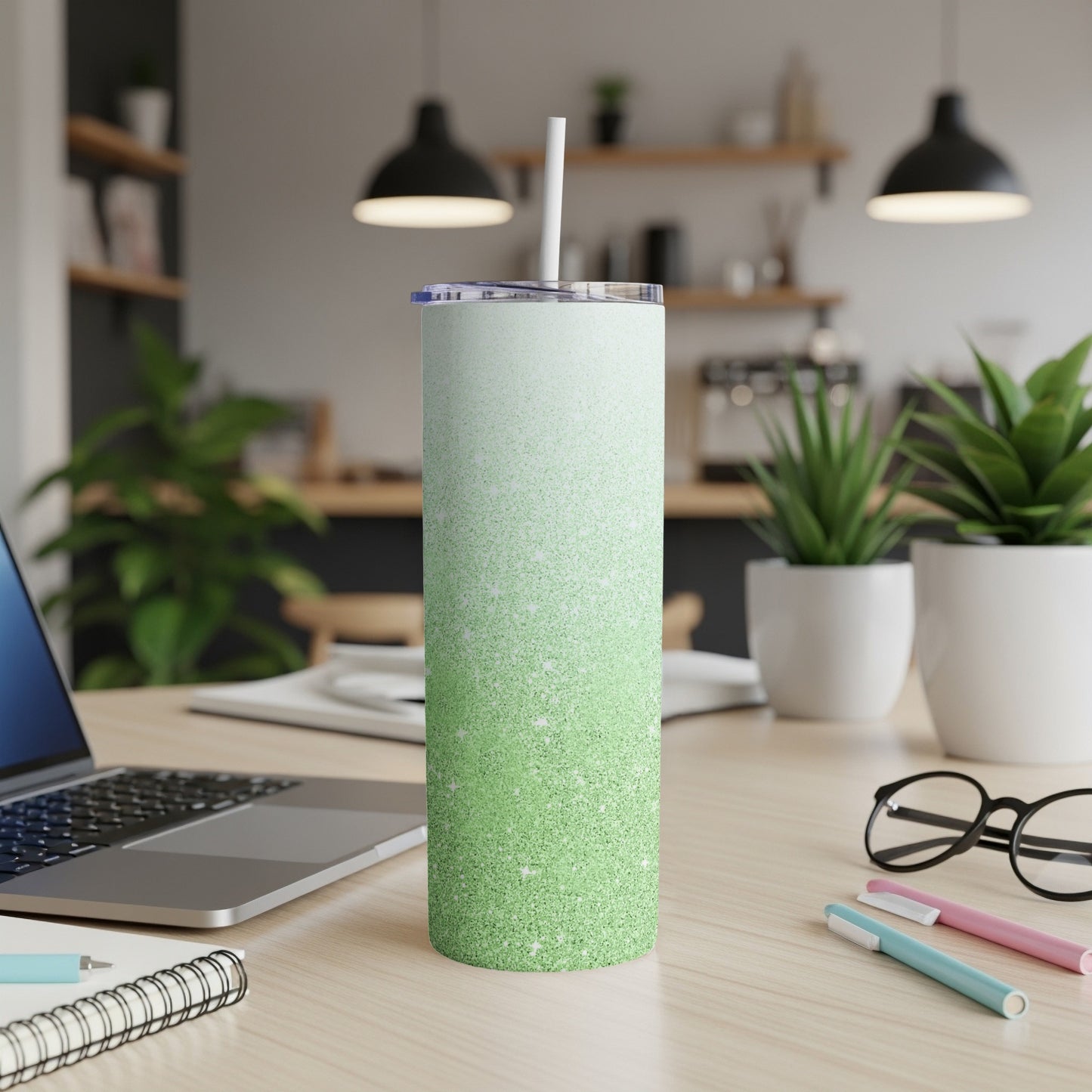 Green glitter tumbler with straw on a desk with a laptop and pens.