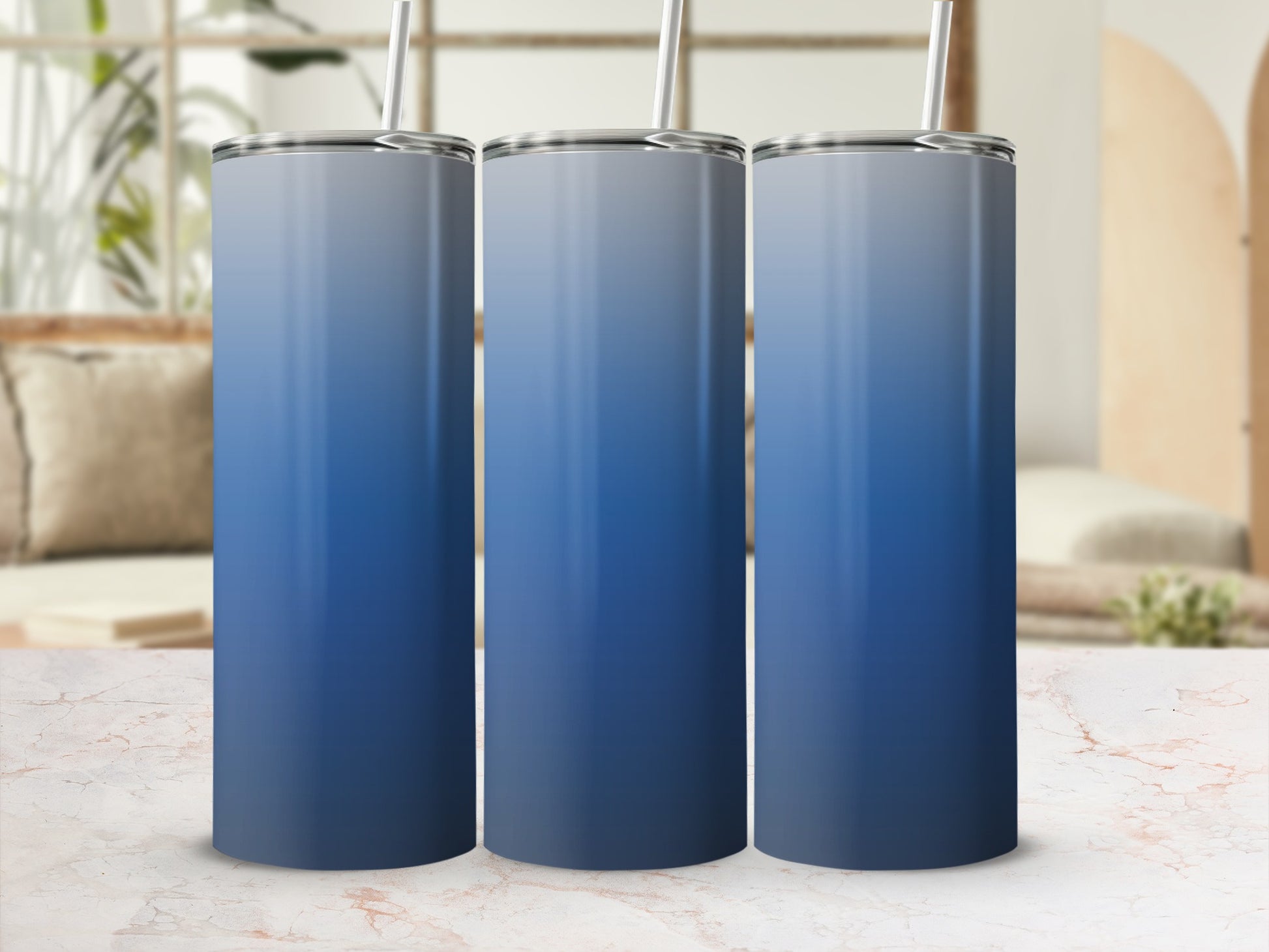 Three gradient blue tumblers with straws on a marble surface.