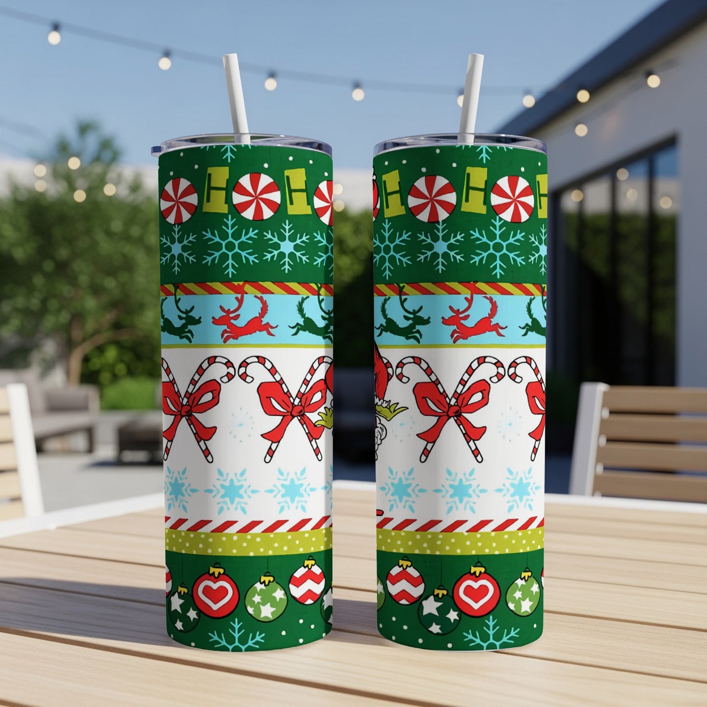 Two Christmas-themed tumblers with candy canes, snowflakes, and reindeer on a patio table.