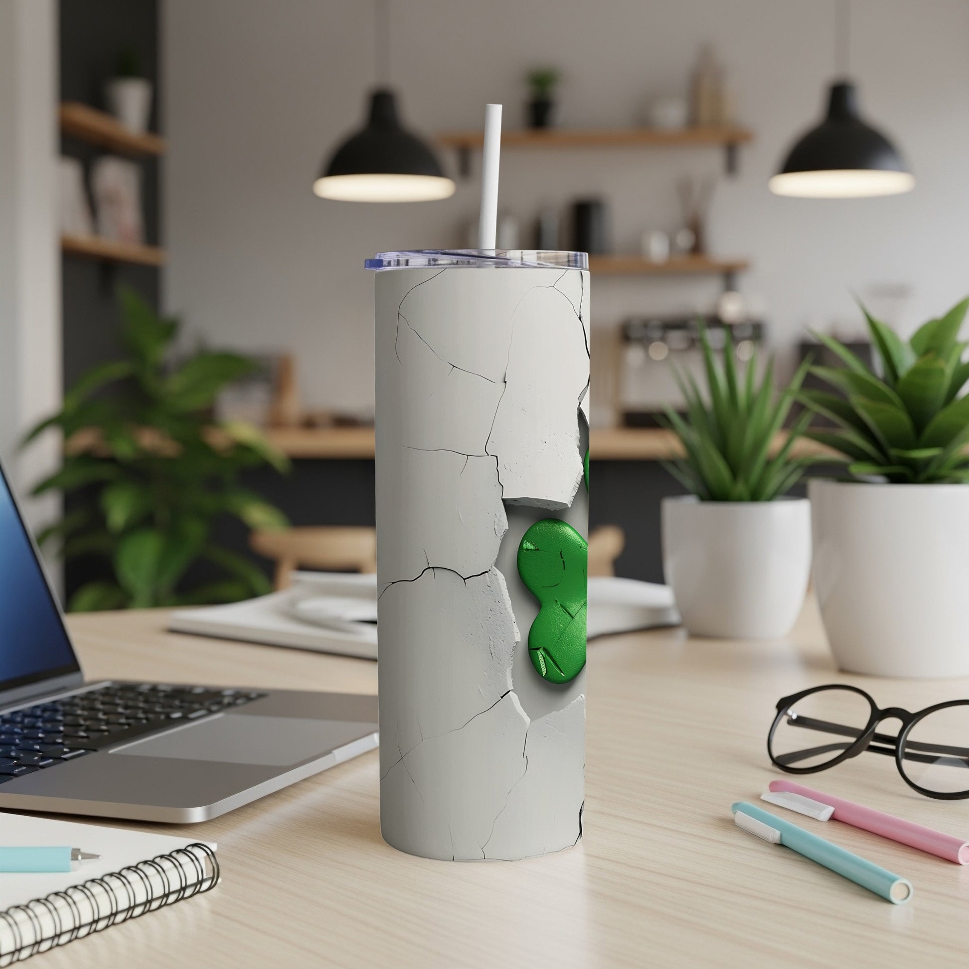 White cracked tumbler with green alien graphic and straw on desk.
