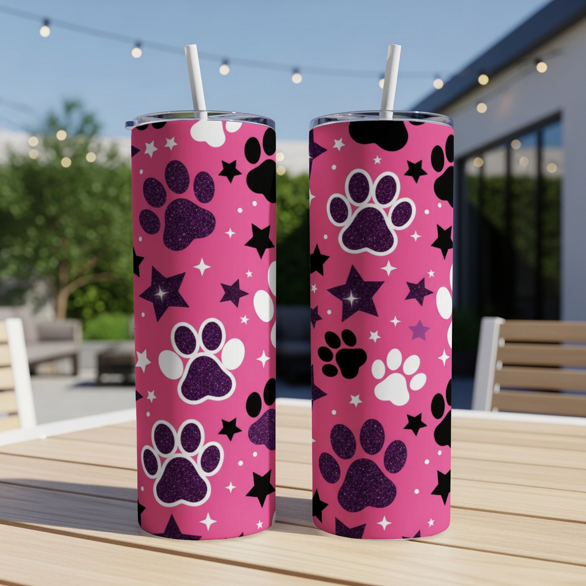 Two pink tumblers with paw prints and stars, set on a table.