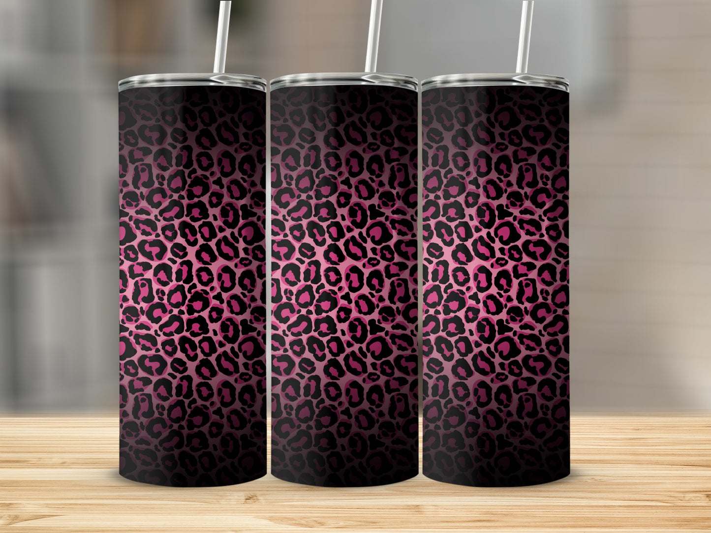Three pink and black leopard print tumblers with white straws on a wooden surface.