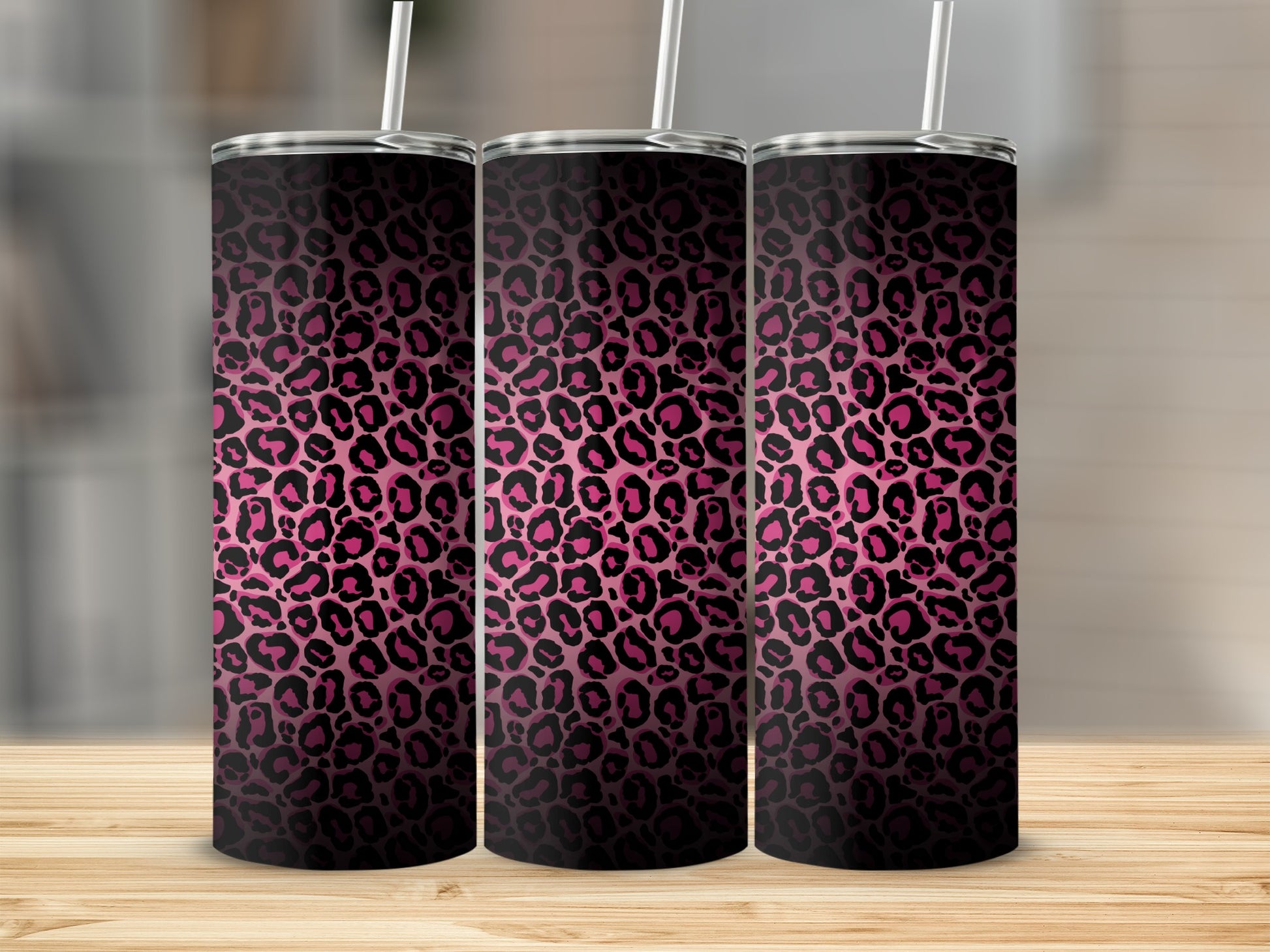 Three pink and black leopard print tumblers with white straws on a wooden surface.