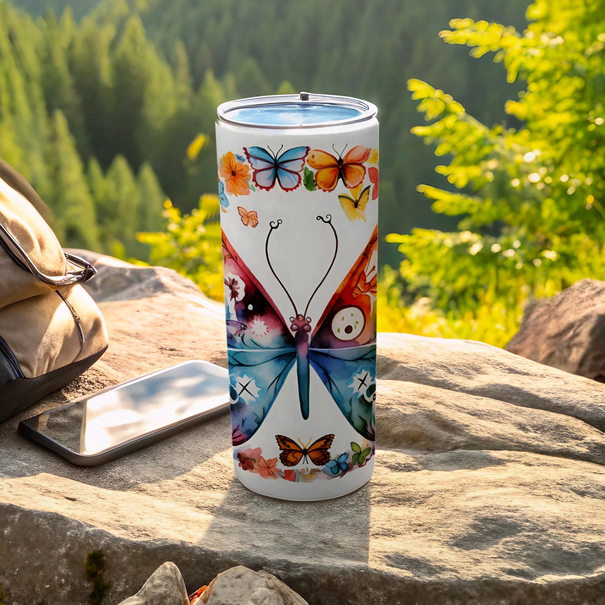 Tumbler with a colorful butterfly design on a rock with a backpack and phone.