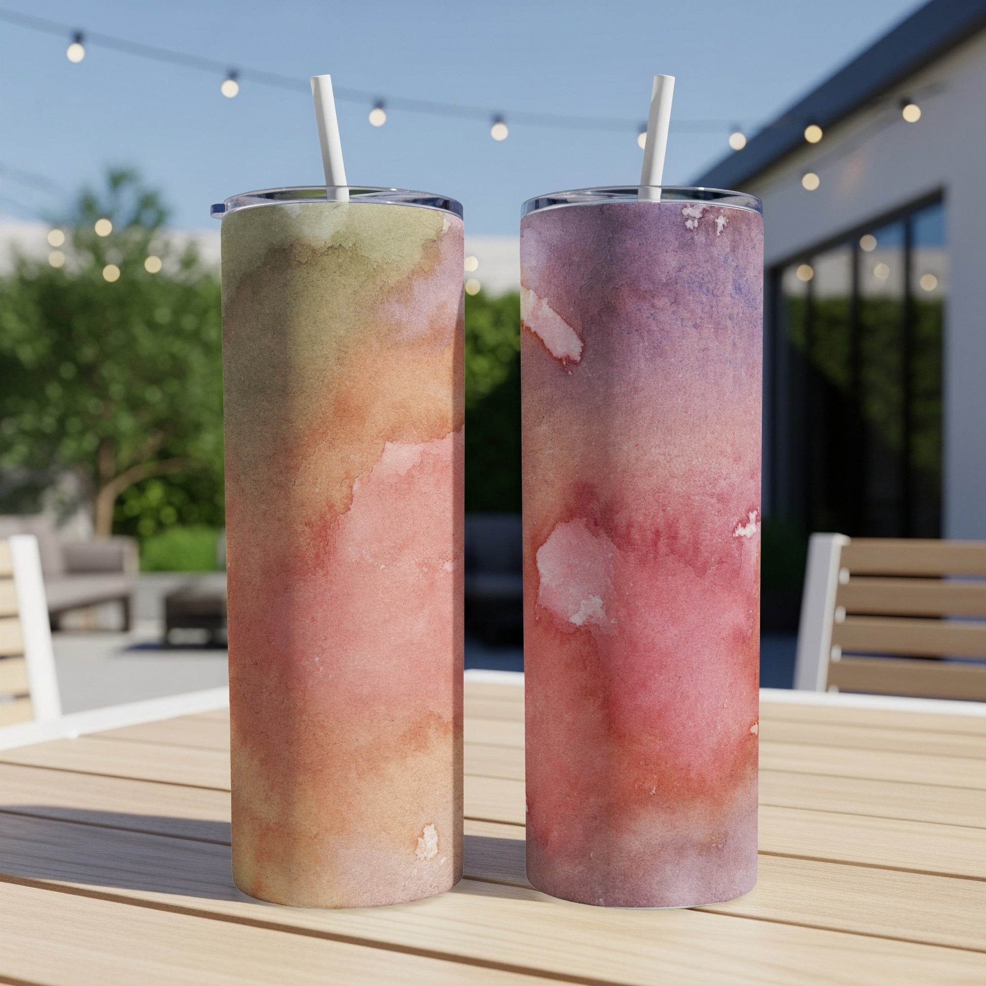 Two tumblers with watercolor designs on a wooden table outdoors.