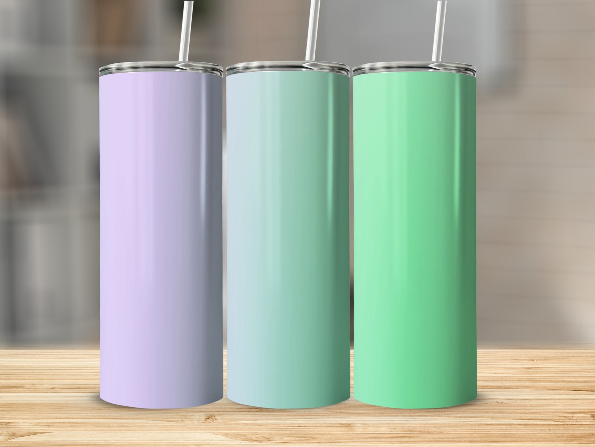 Three blank pastel colored tumblers with straws stand on a wooden surface.