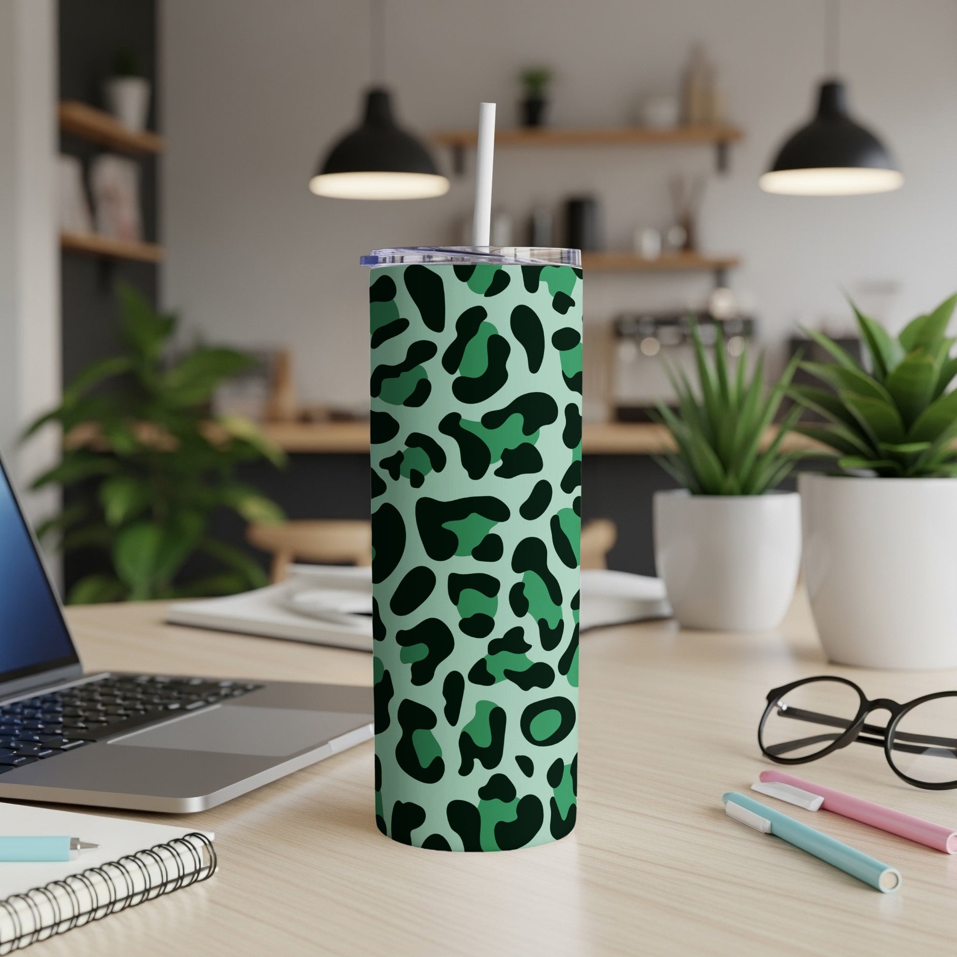 Green leopard print tumbler with straw on a wooden desk.