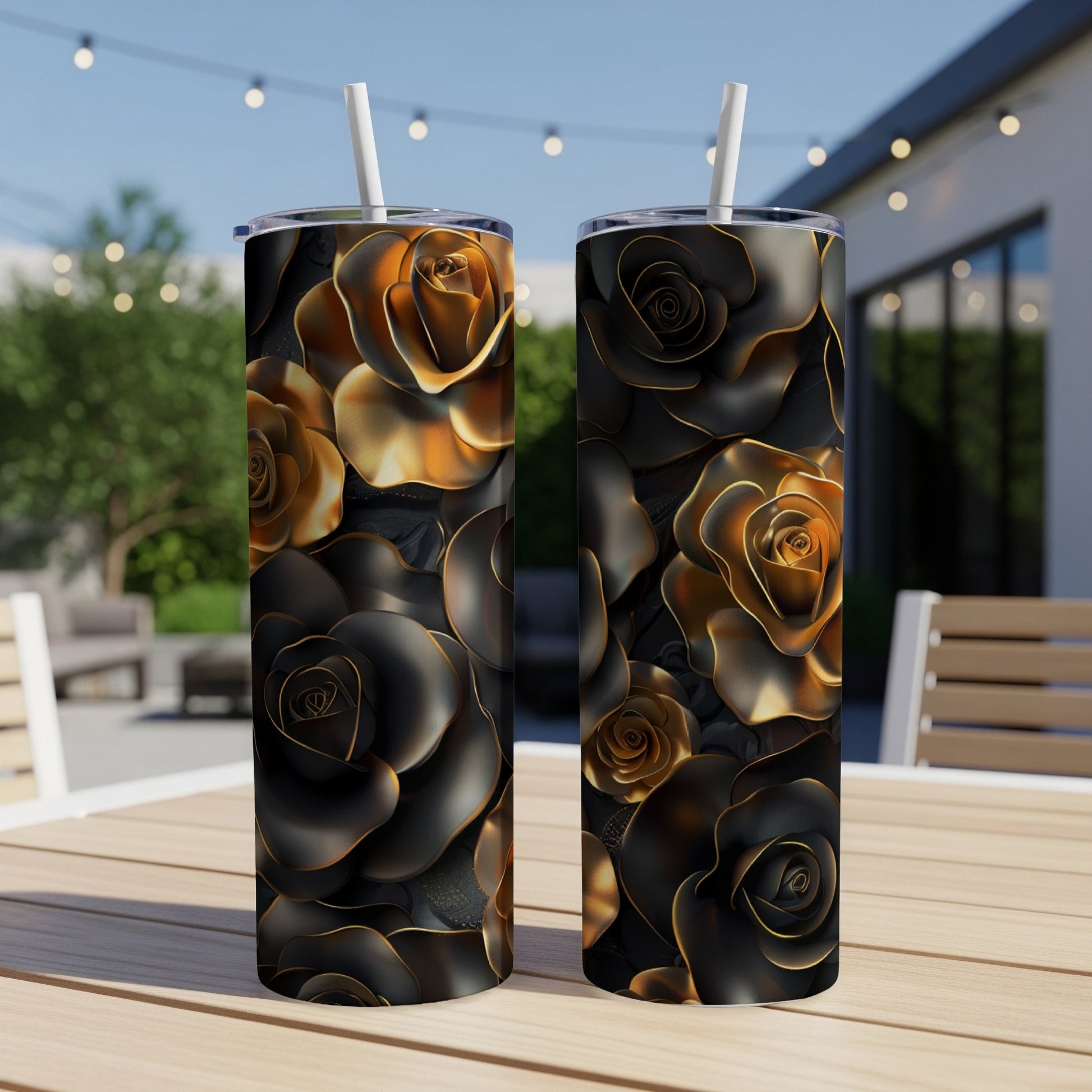 Two black and gold rose pattern tumblers with straws on a wooden table outdoors.