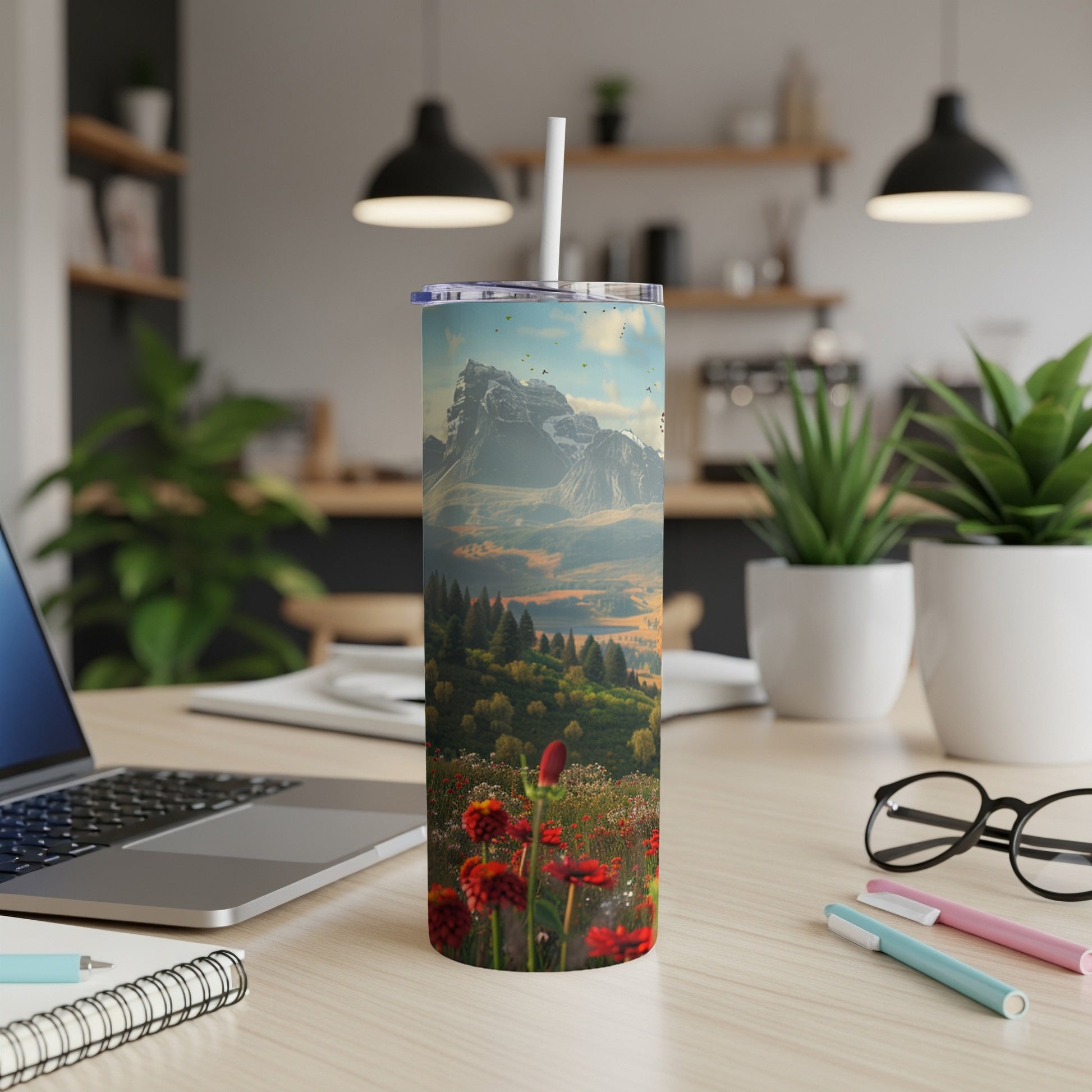 Tumbler with mountain landscape and red wildflowers on desk.