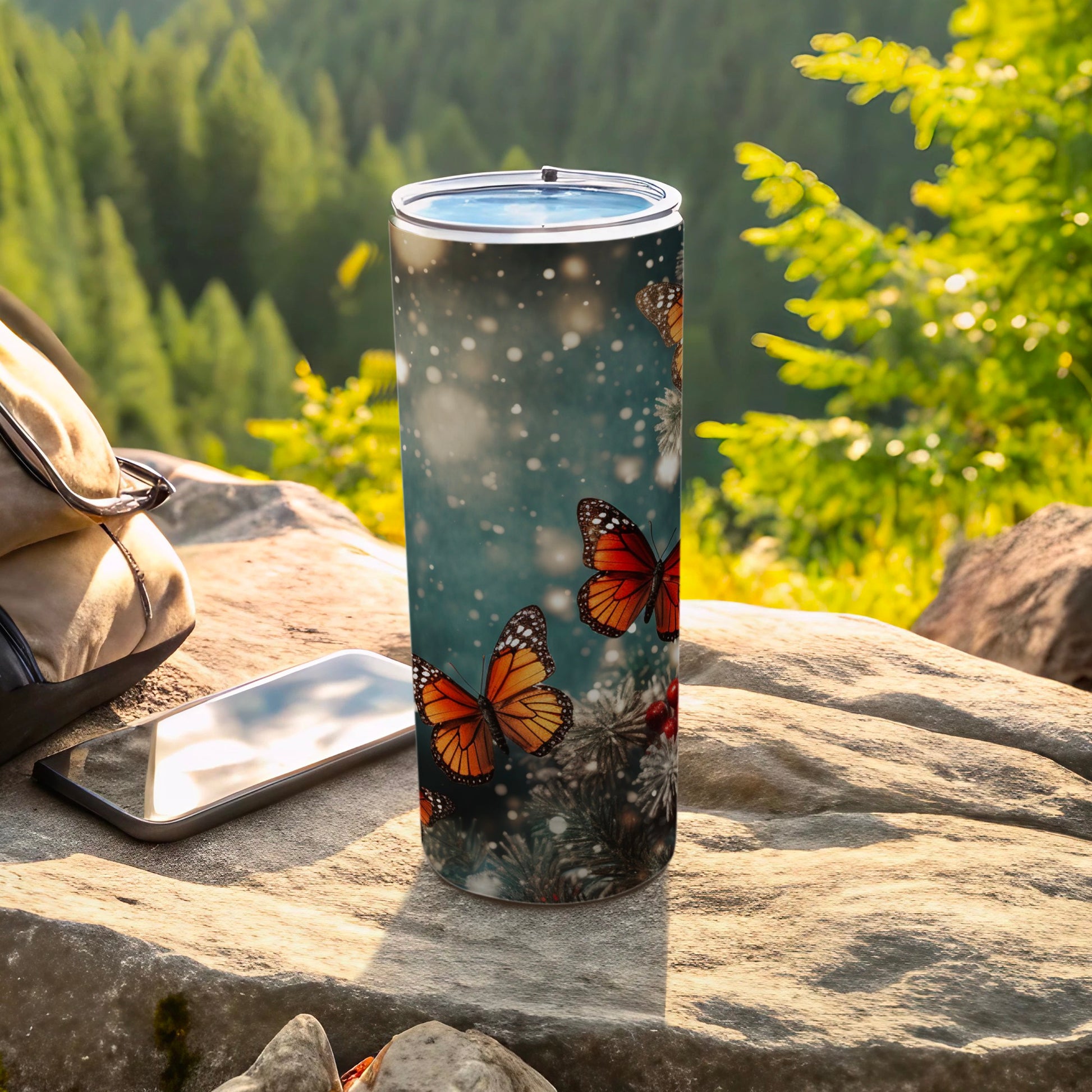 Tumbler with monarch butterflies and pine branches on a rocky surface.