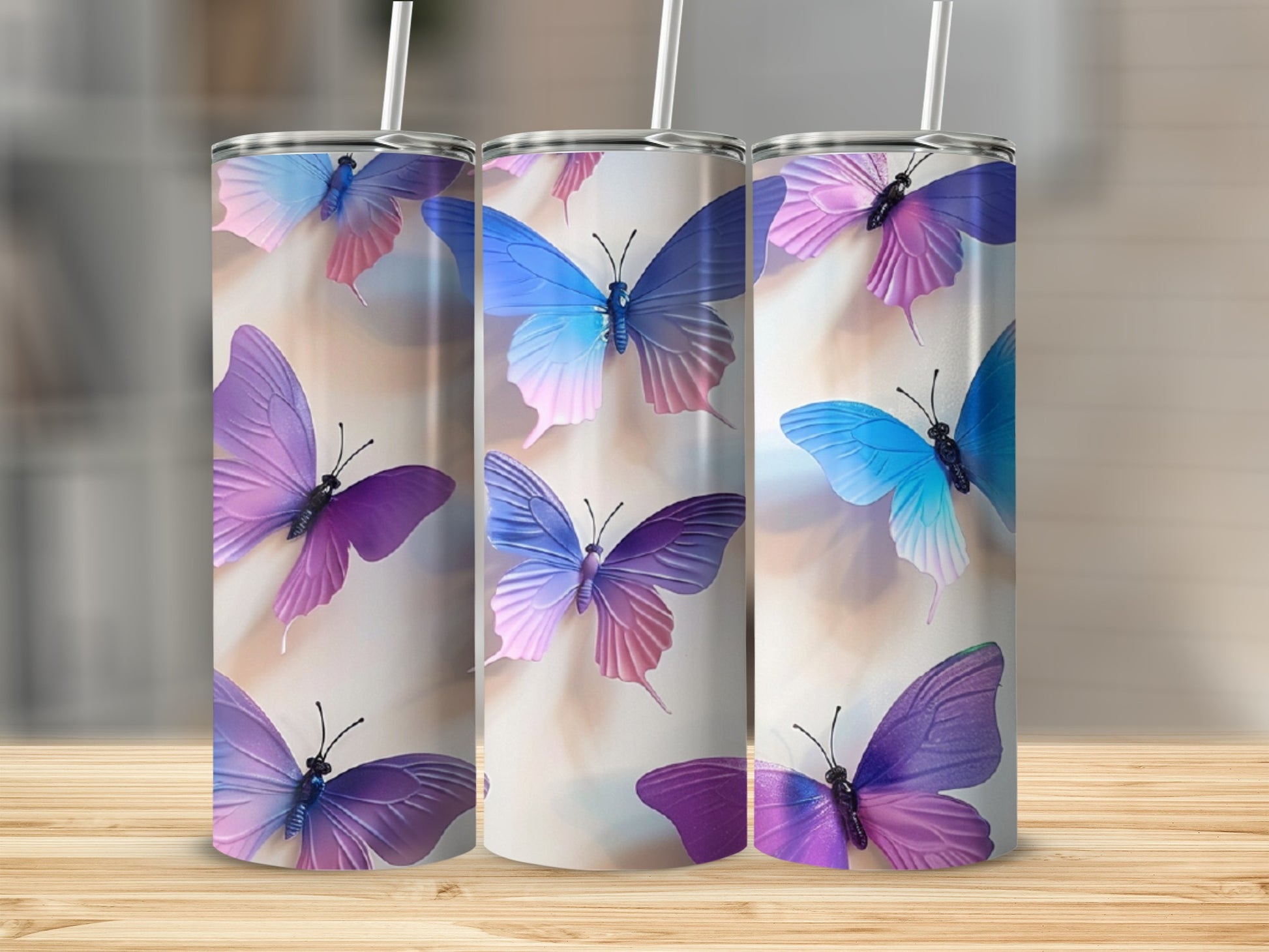 Three tumblers with colorful butterfly designs on a wooden surface.