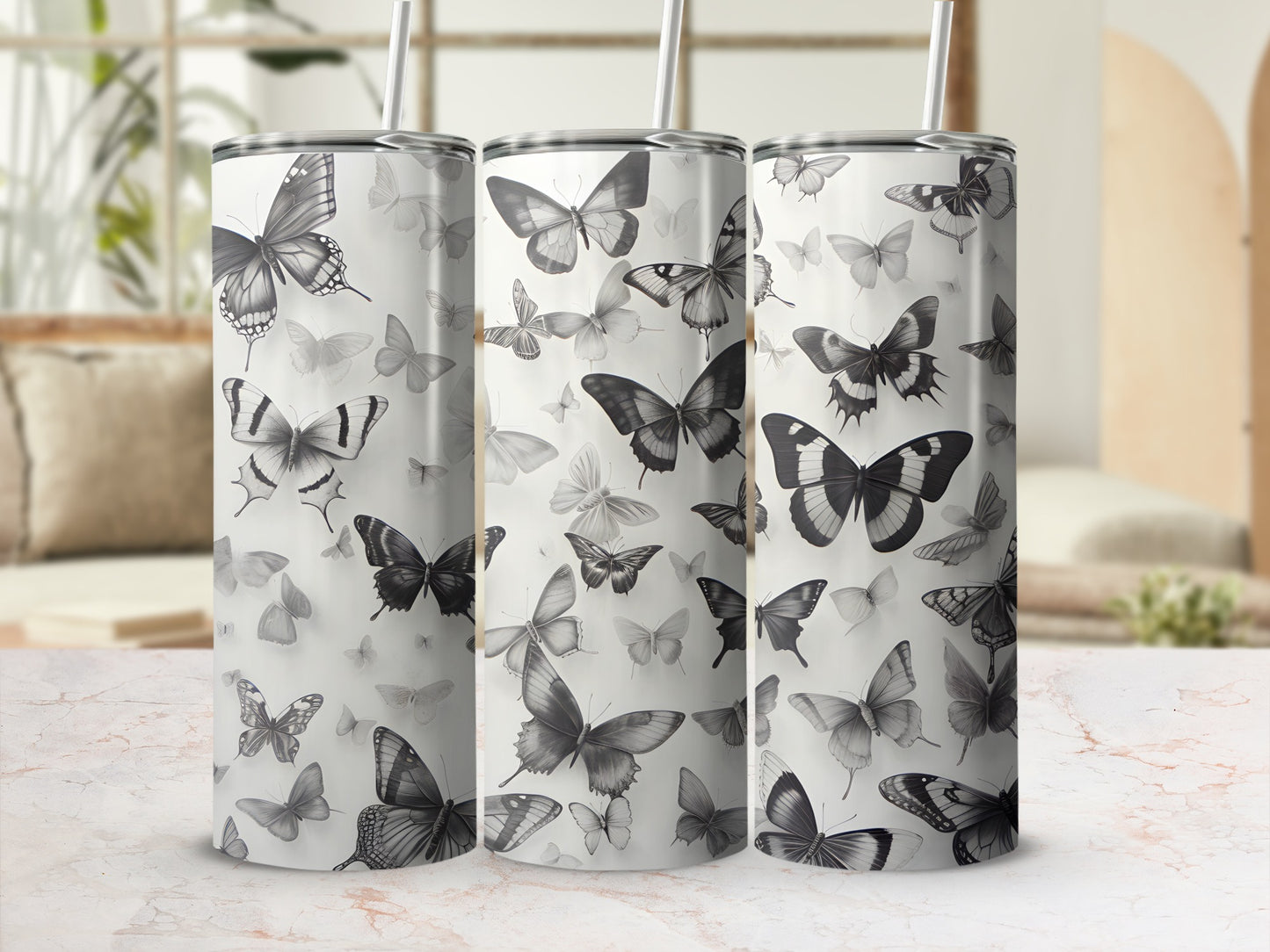 Three tumblers with a grayscale butterfly pattern against a blurred background.