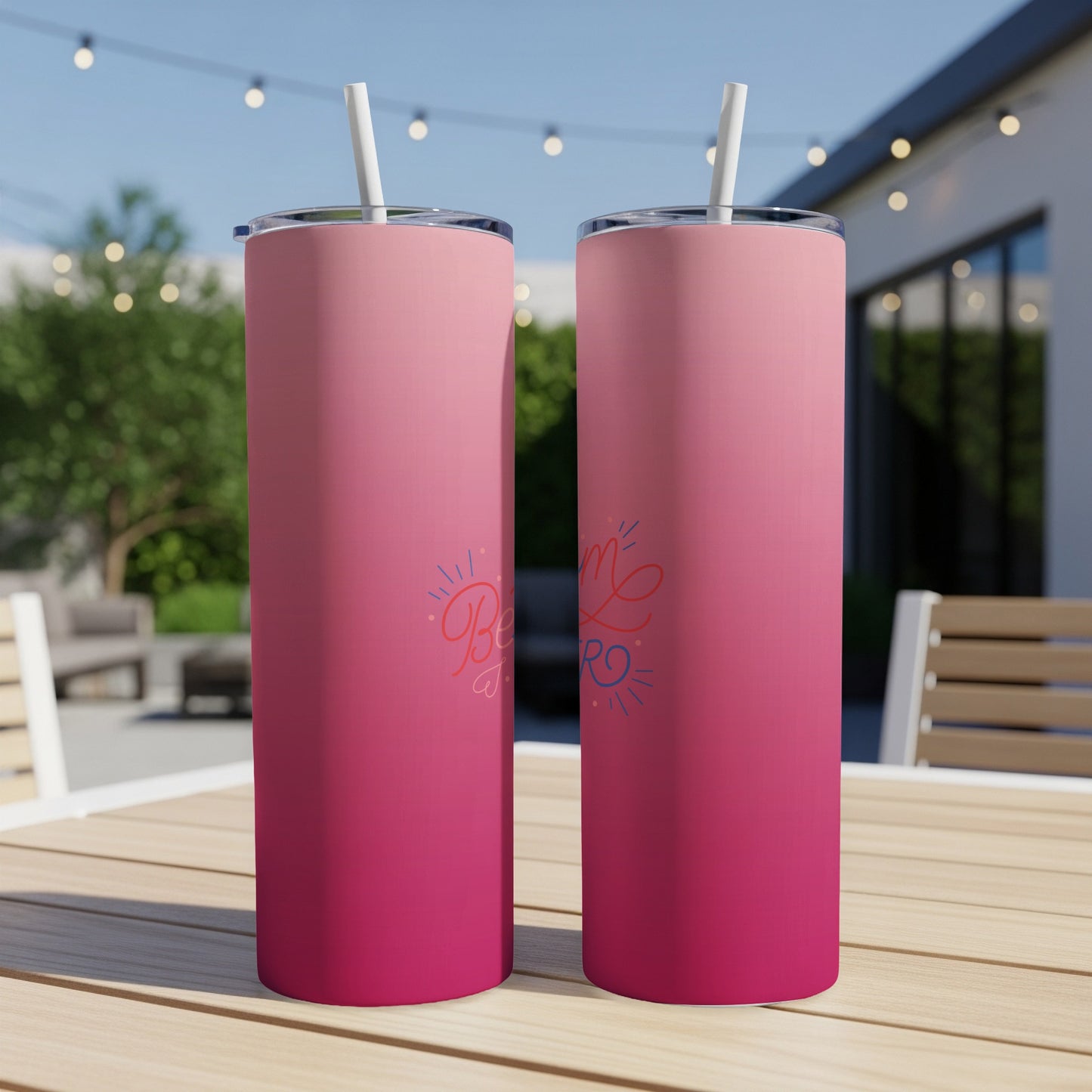 Pink gradient tumbler with "Be Kind" text and straw on outdoor table.