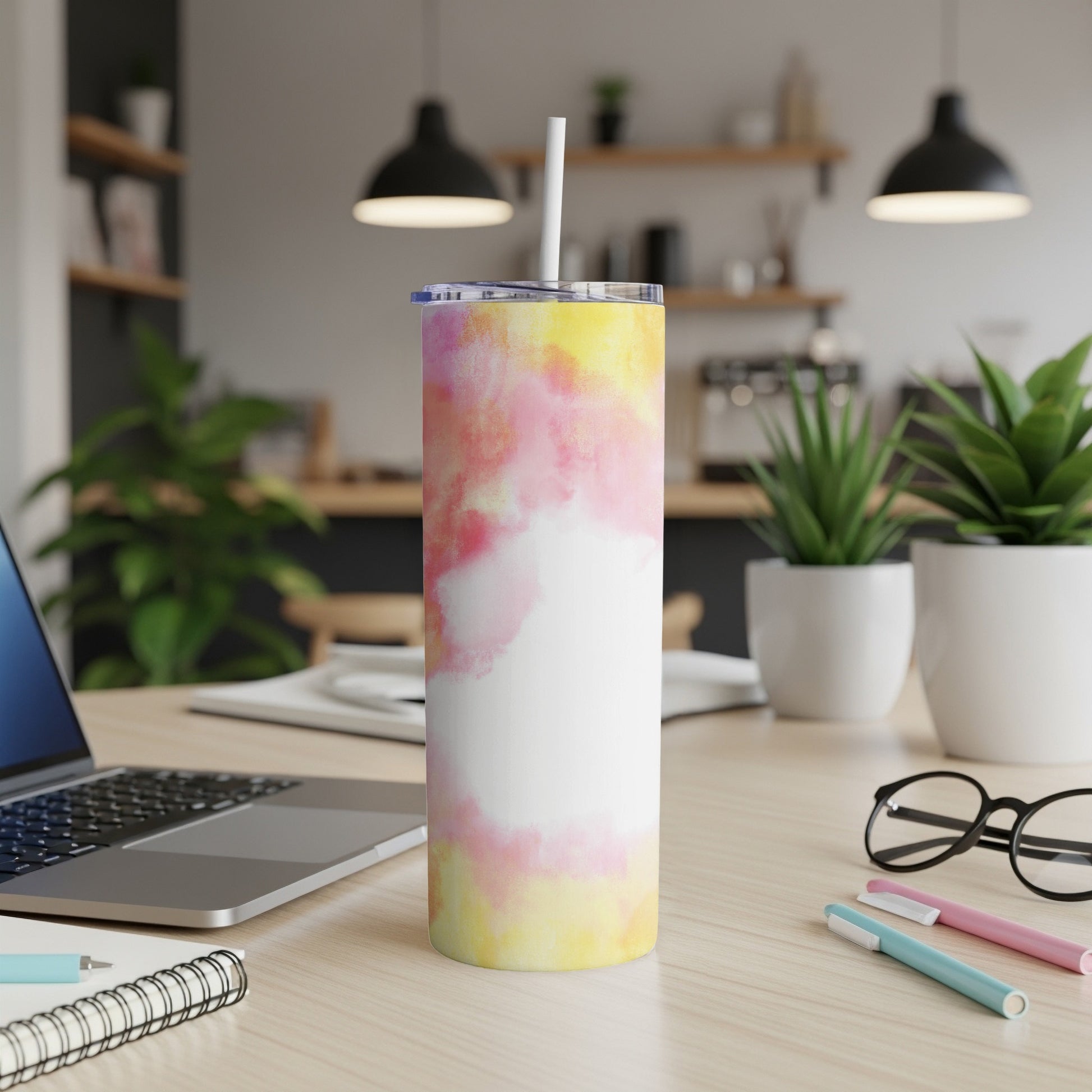 Tall tumbler with abstract yellow and pink watercolor design on desk.