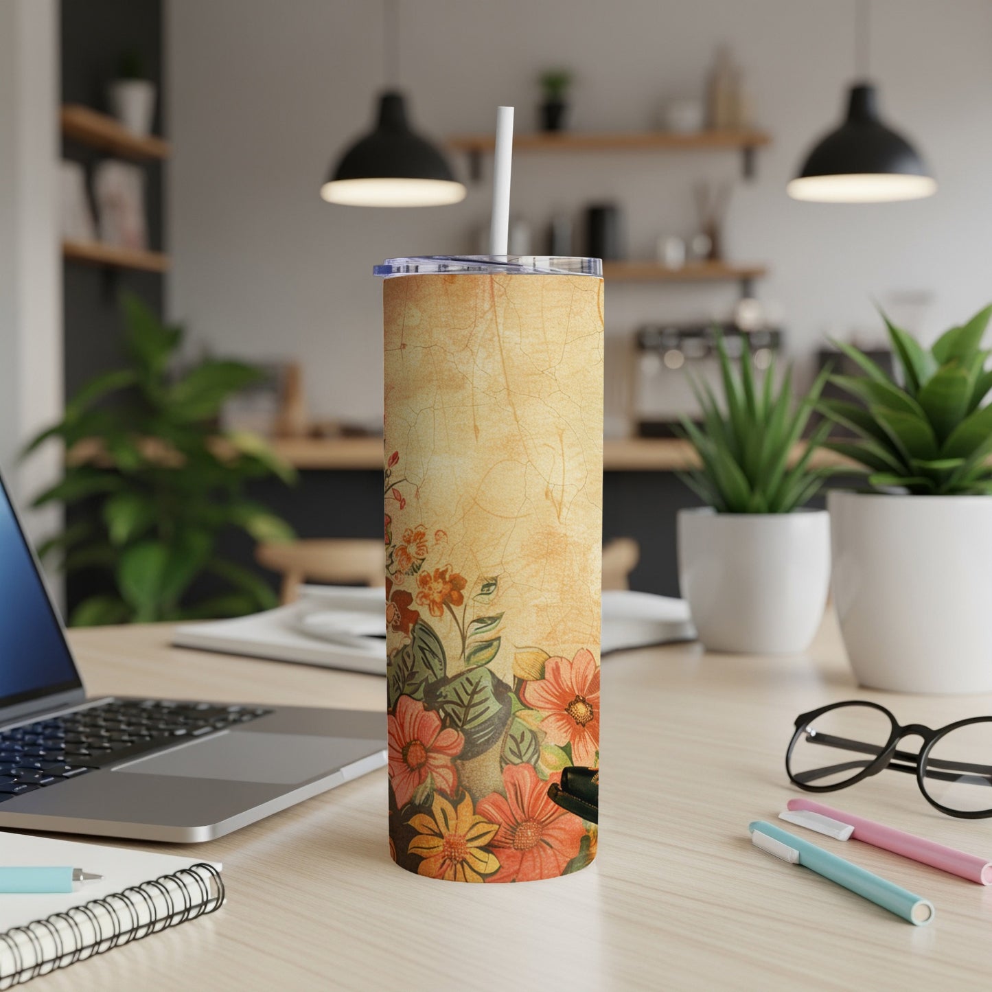 Floral patterned tumbler with straw on a desk next to a laptop.
