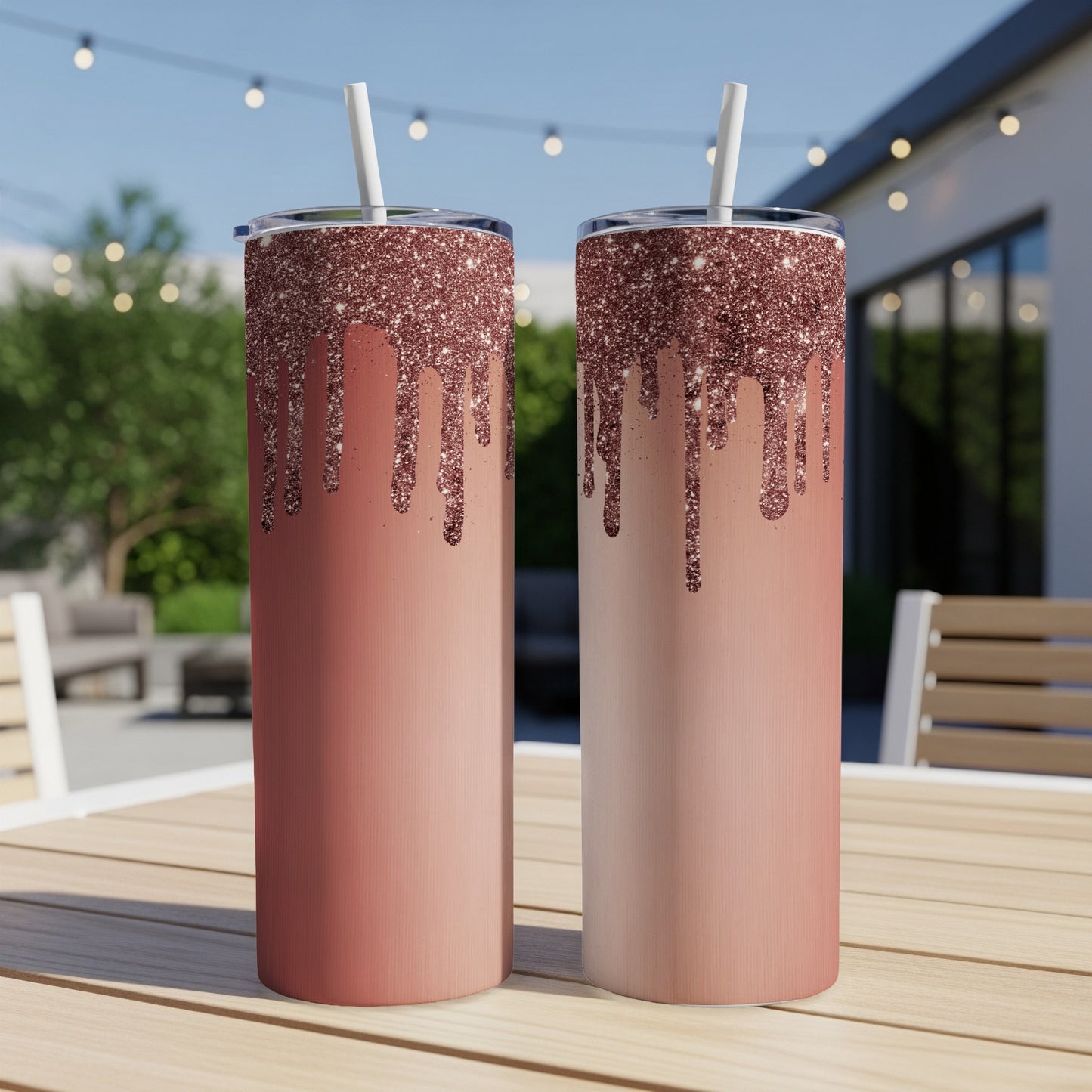 Two tall tumblers with rose gold glitter drip design stand on a wooden table outdoors.