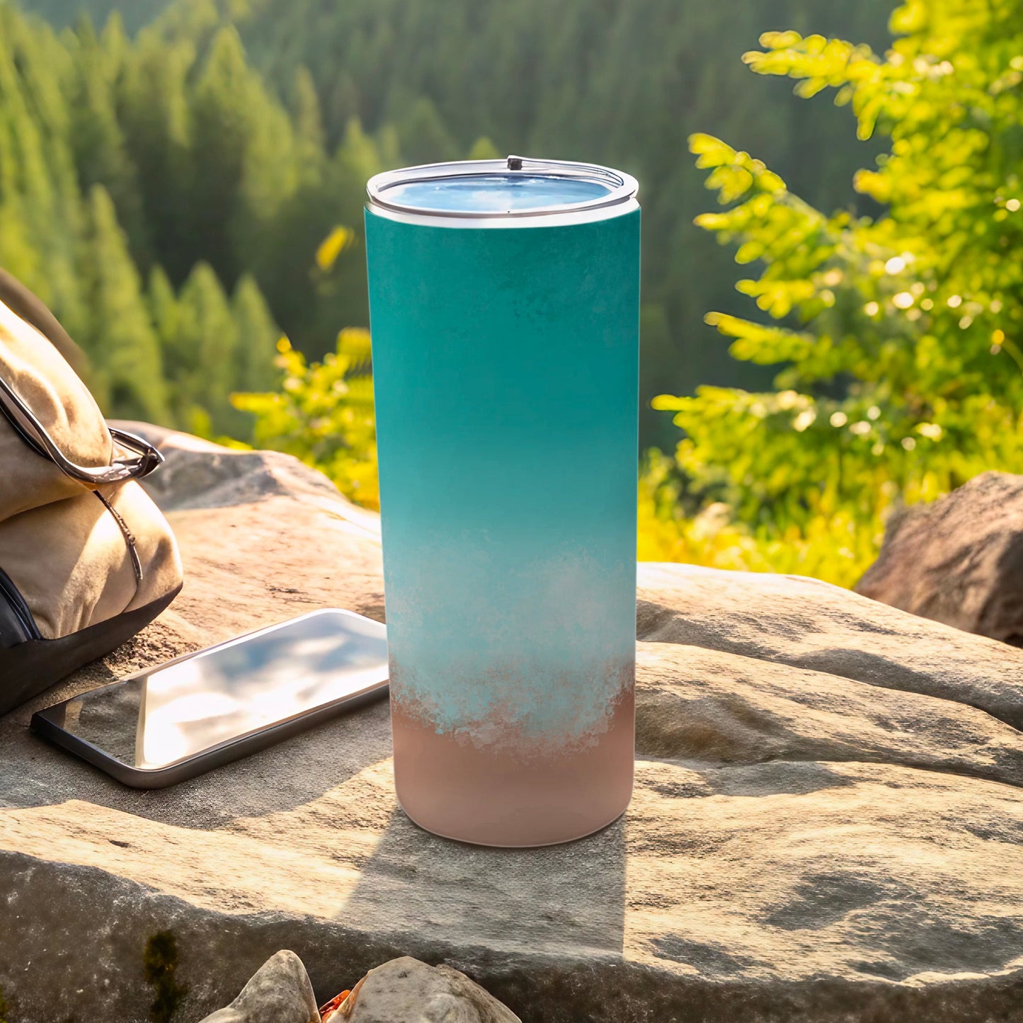 Gradient teal and beige tumbler on rock with phone and backpack.