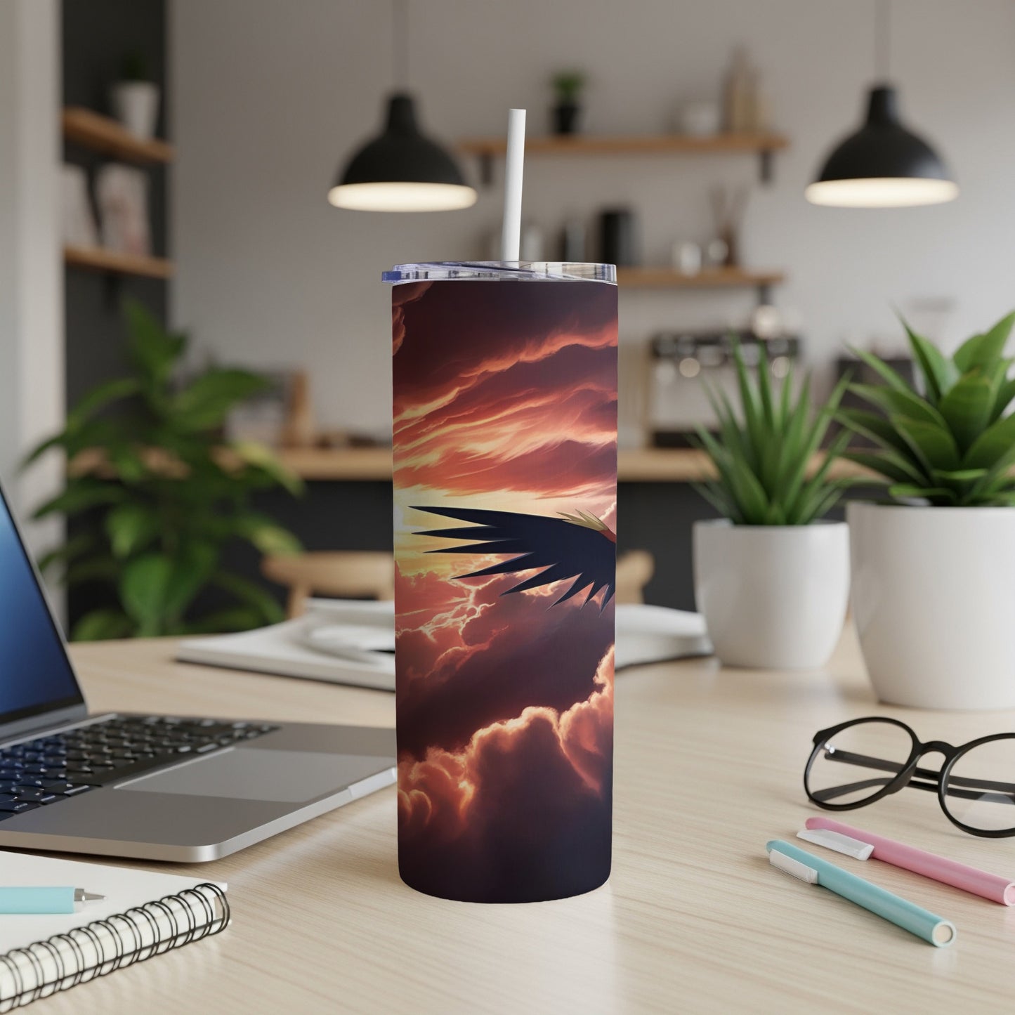 Tall tumbler with angel wing and sky graphic, on desk with laptop.