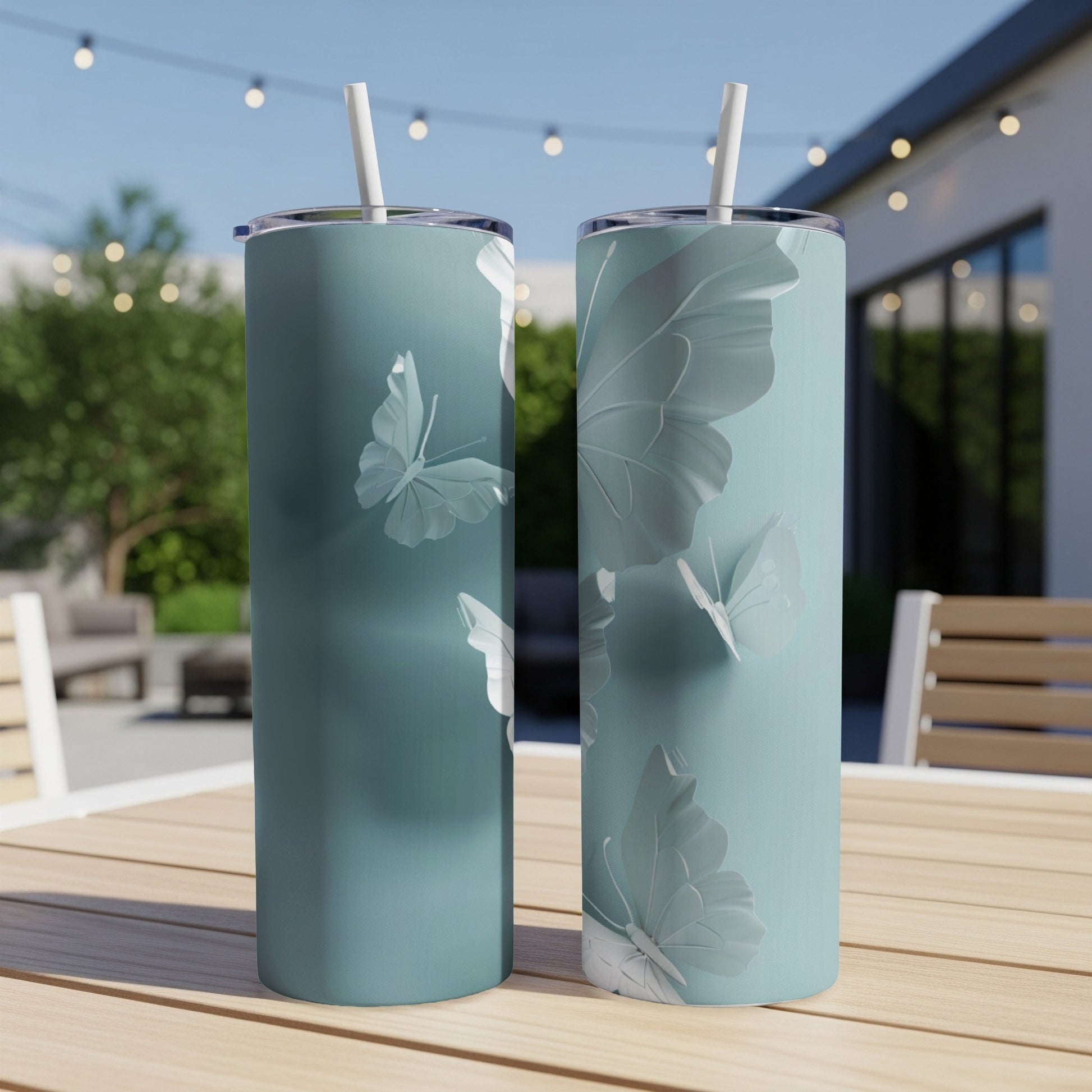 Two light teal tumblers with embossed white butterflies on a wooden table.