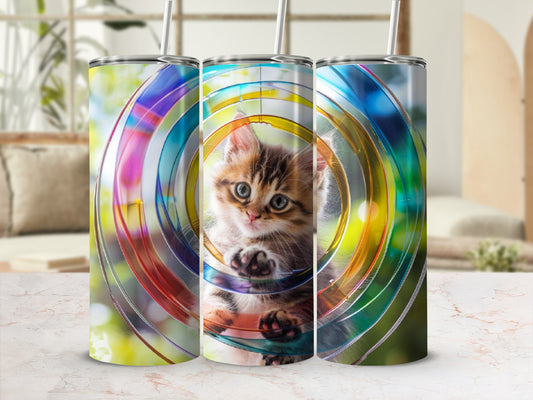 Kitten playing in colorful concentric circles on a tumbler.