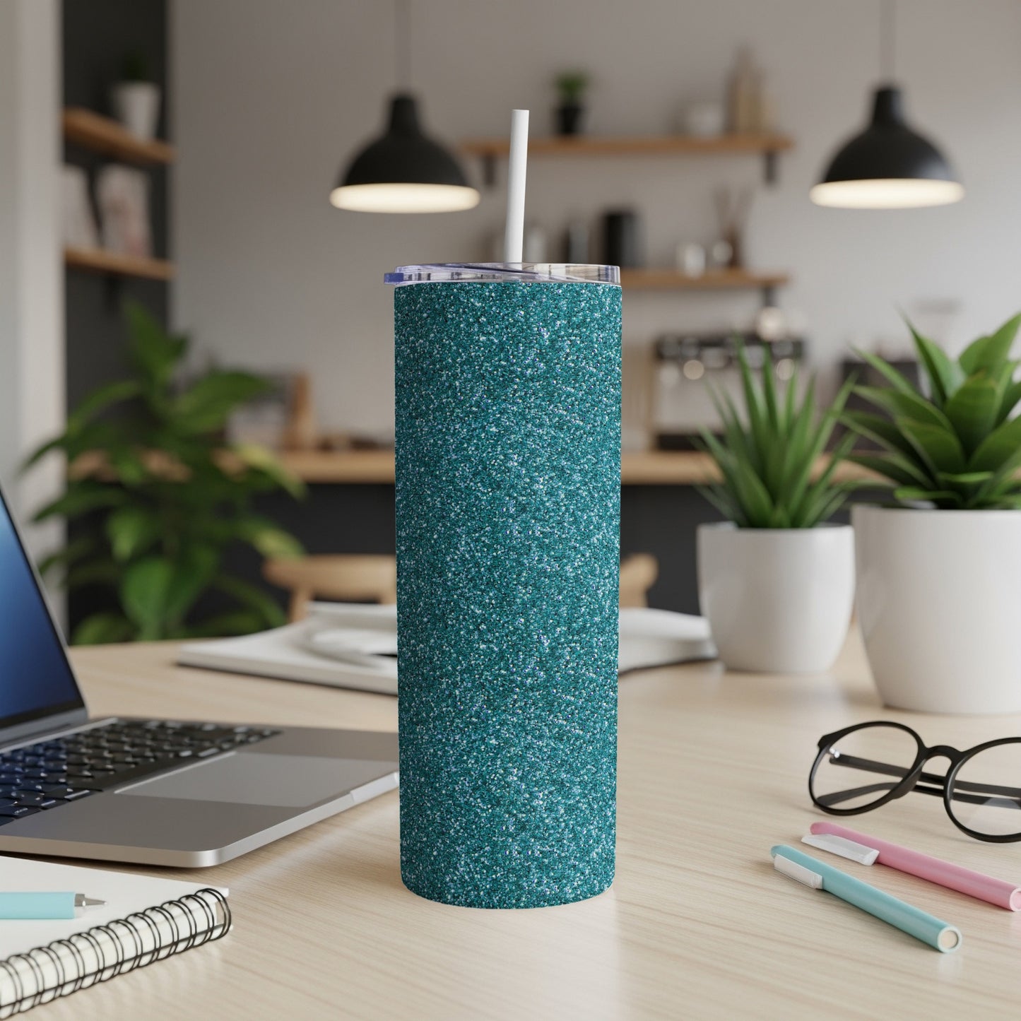 Glitter teal skinny tumbler with white straw and clear lid on a desk.