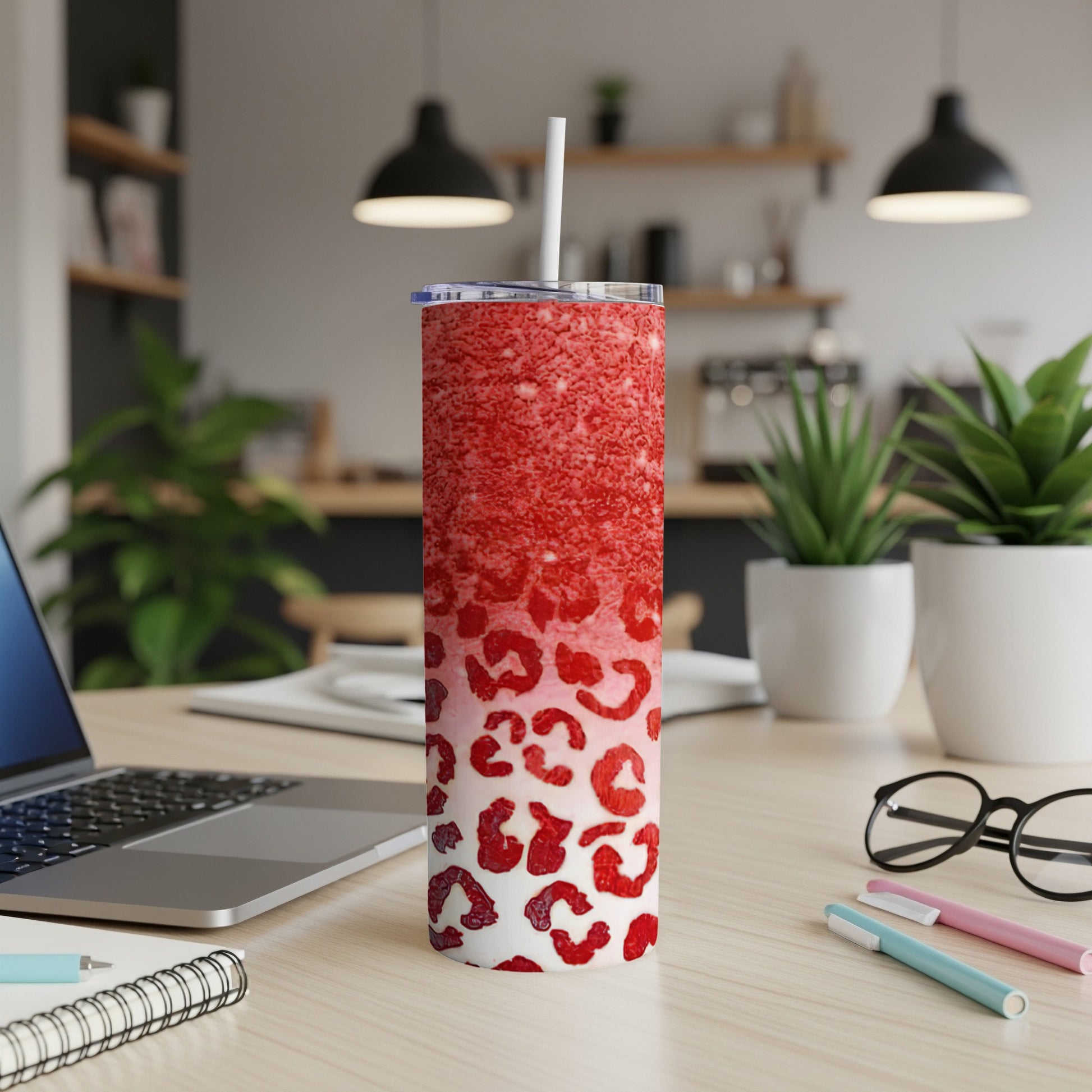 Red glitter tumbler with white leopard print and straw on a desk.