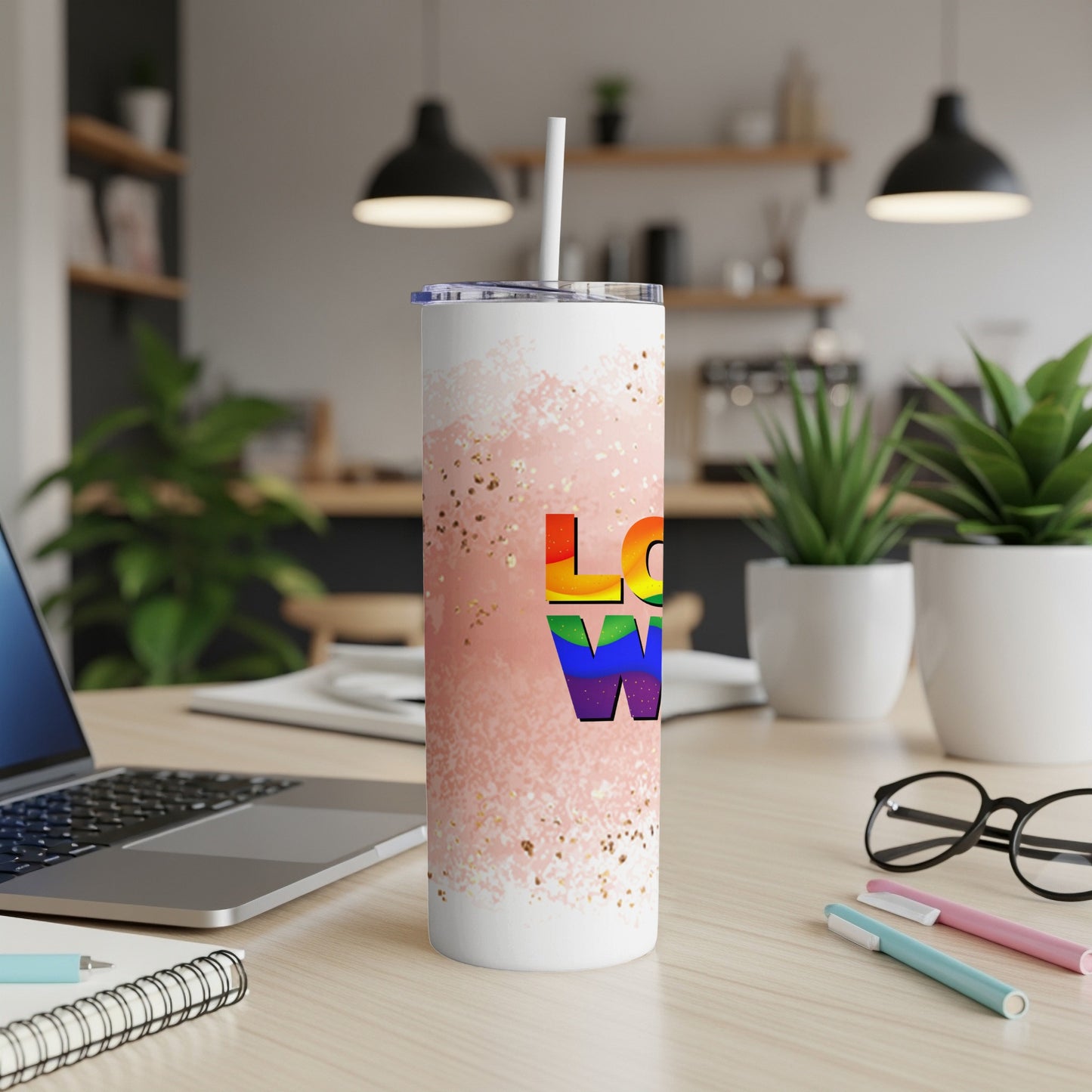Pride rainbow "Love" tumbler with straw on a desk.