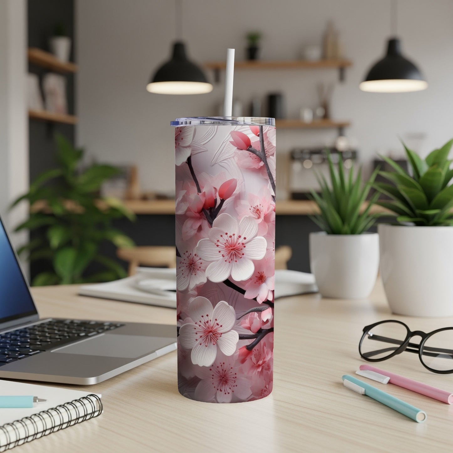 Pink cherry blossoms on a white tumbler with a straw, on a desk.