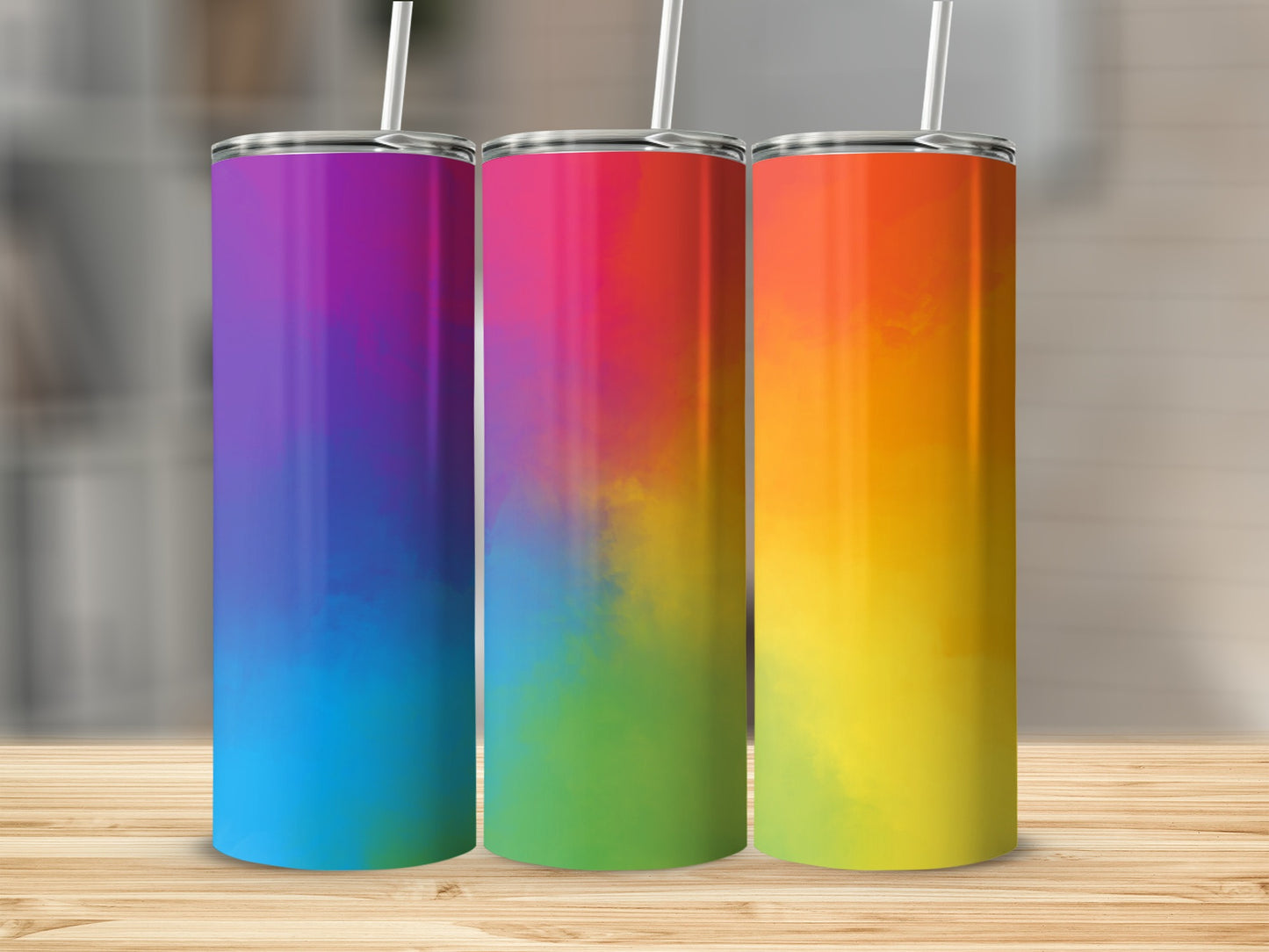 Three tall tumblers with rainbow gradient designs stand on a wooden surface.
