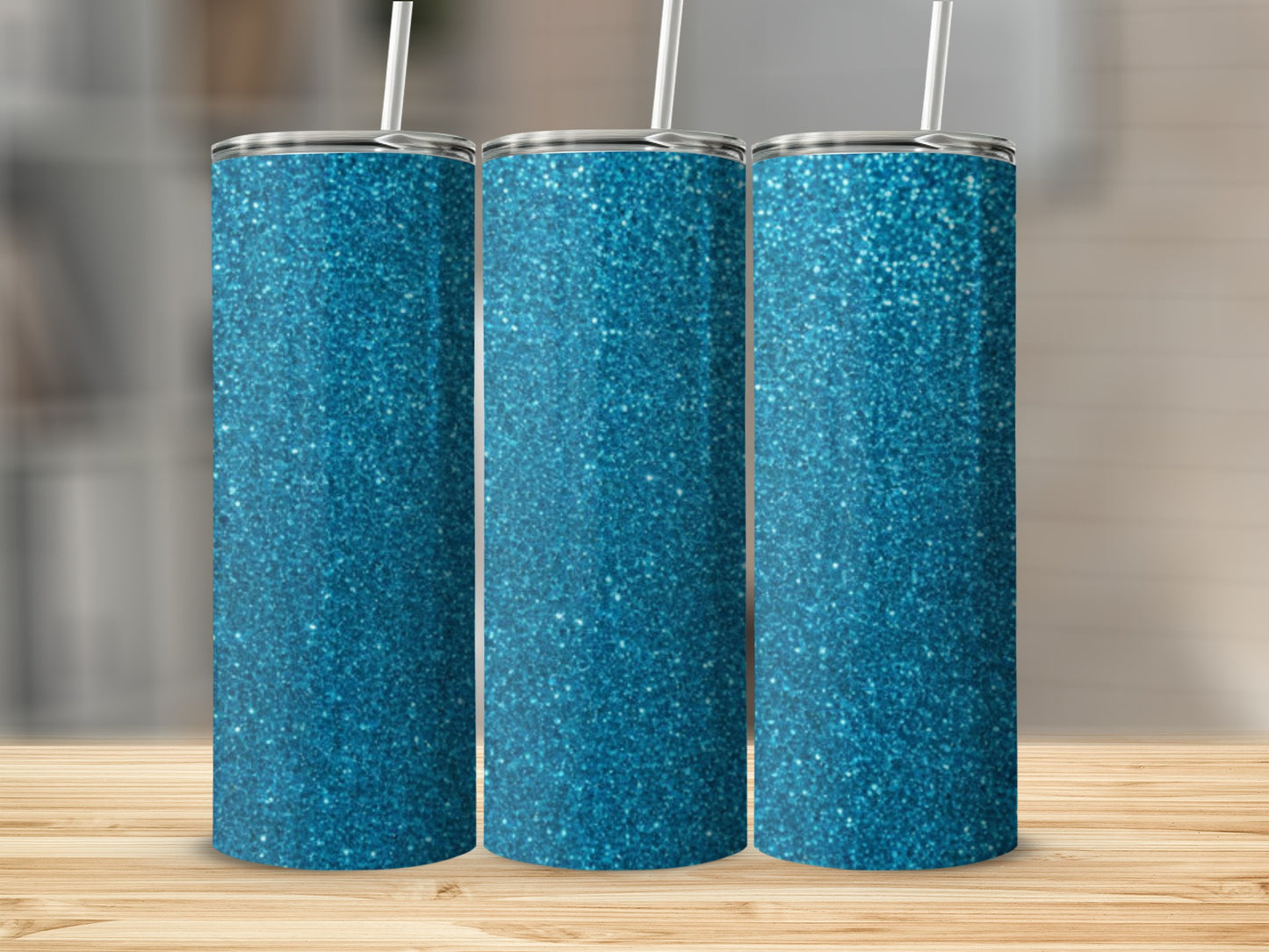 Three glittery blue tumblers with white straws on a wooden surface.
