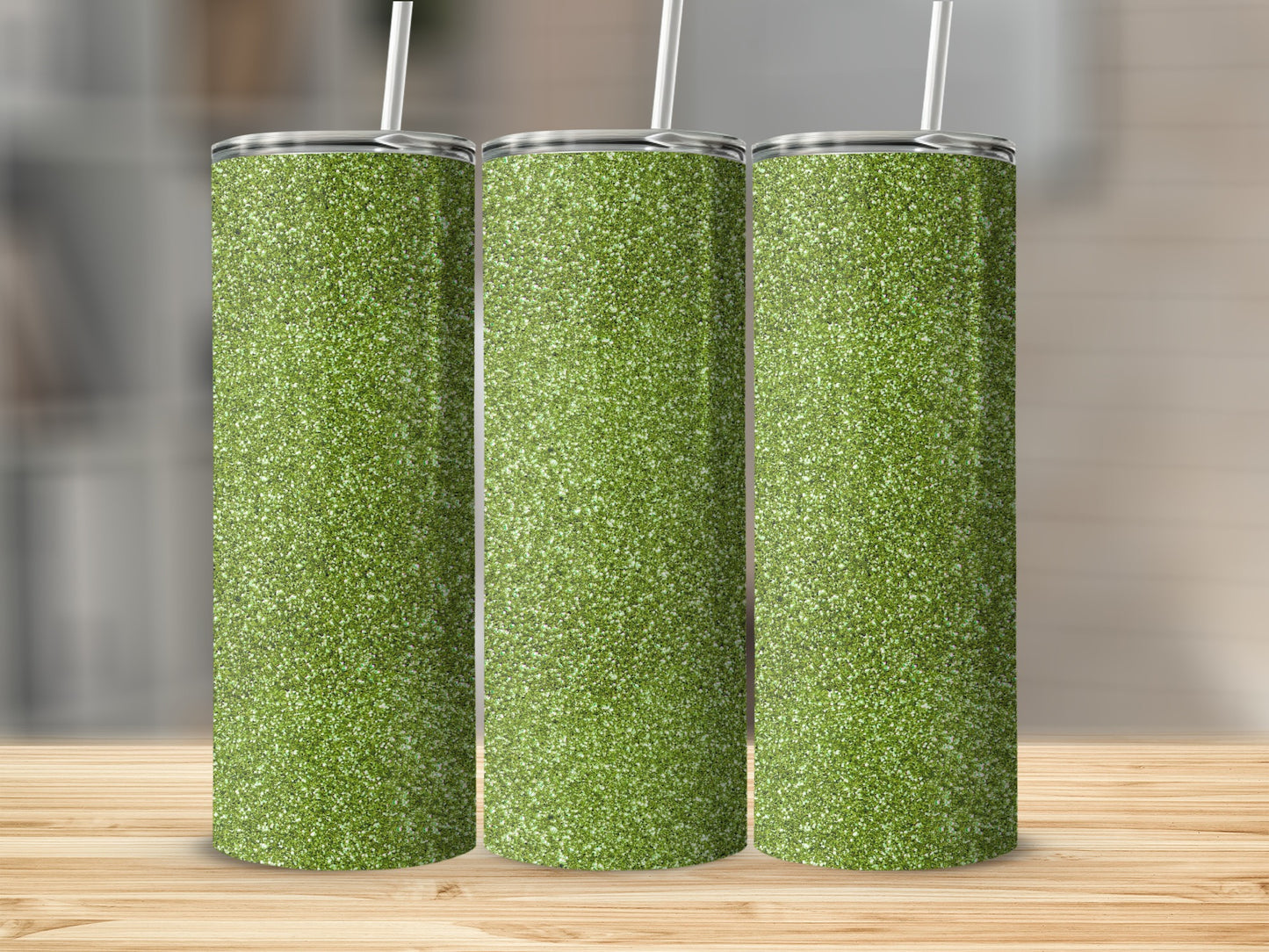 Three tall, glittery green tumblers with straws stand on a wooden table.