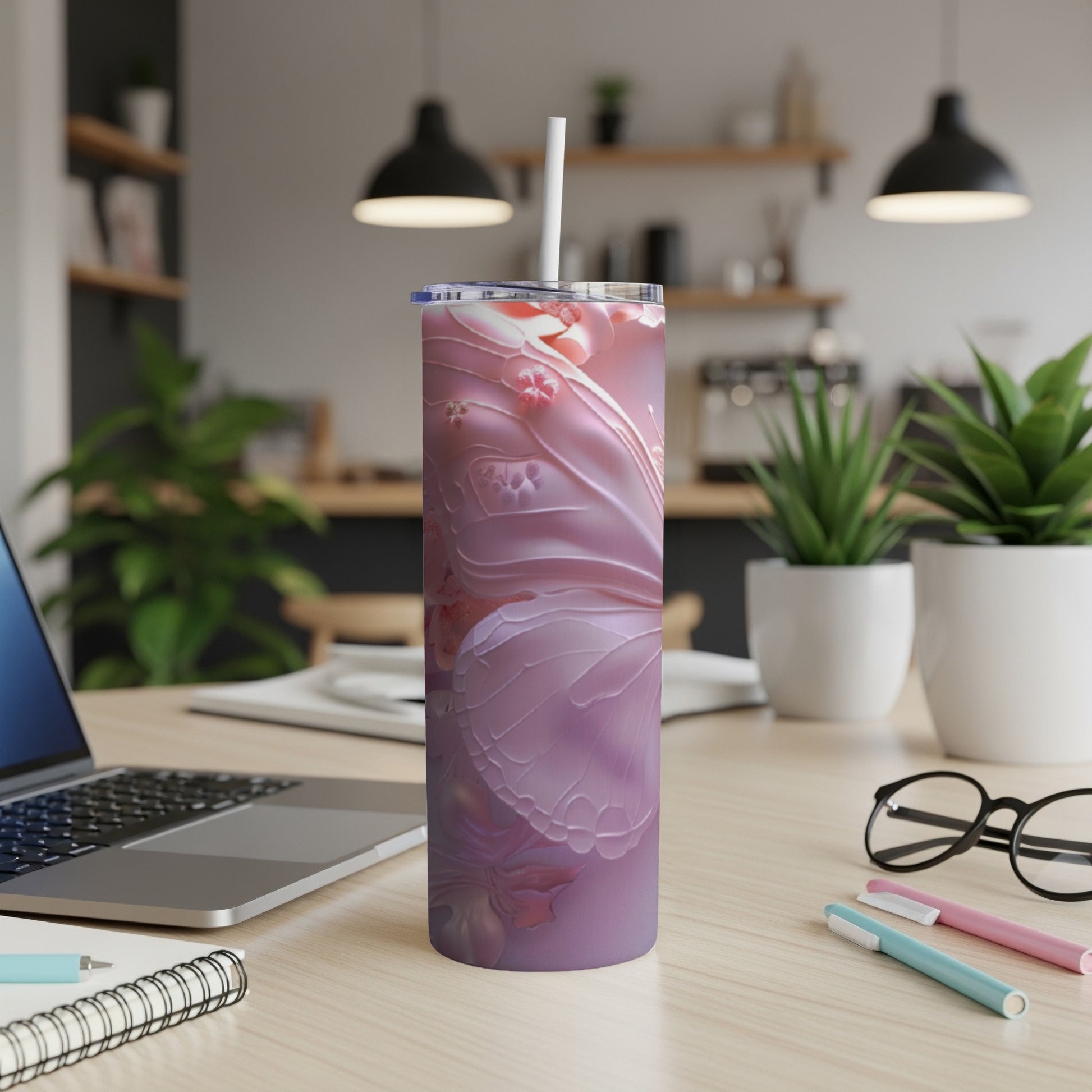 Pink floral design tumbler with straw on a desk with laptop and pens.