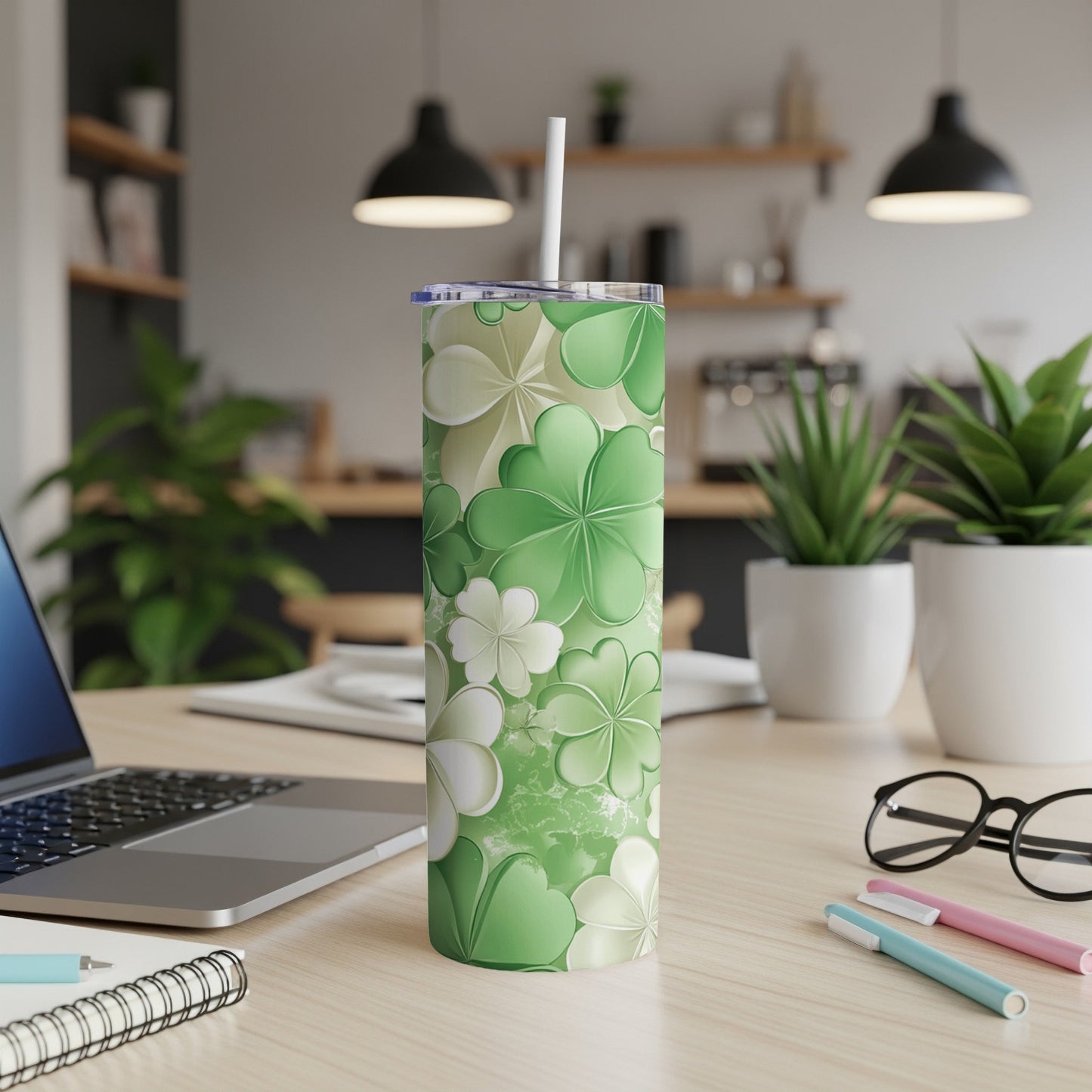 Green floral and shamrock patterned tumbler with white straw on desk.
