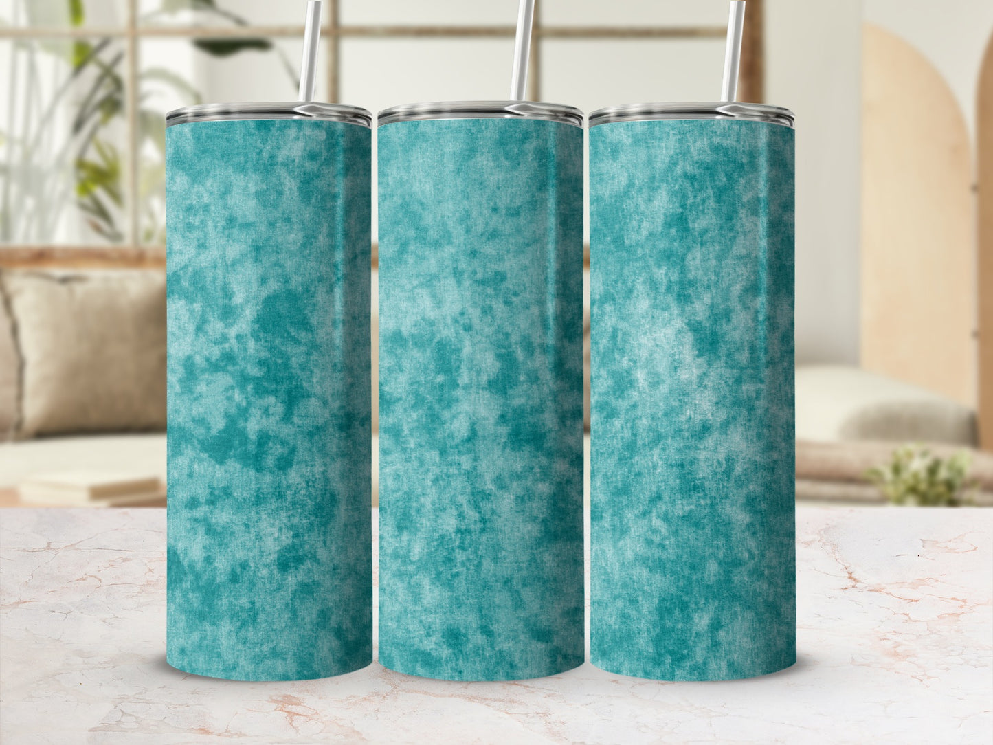 Three teal marbled tumblers with metal lids and straws on a marble surface.