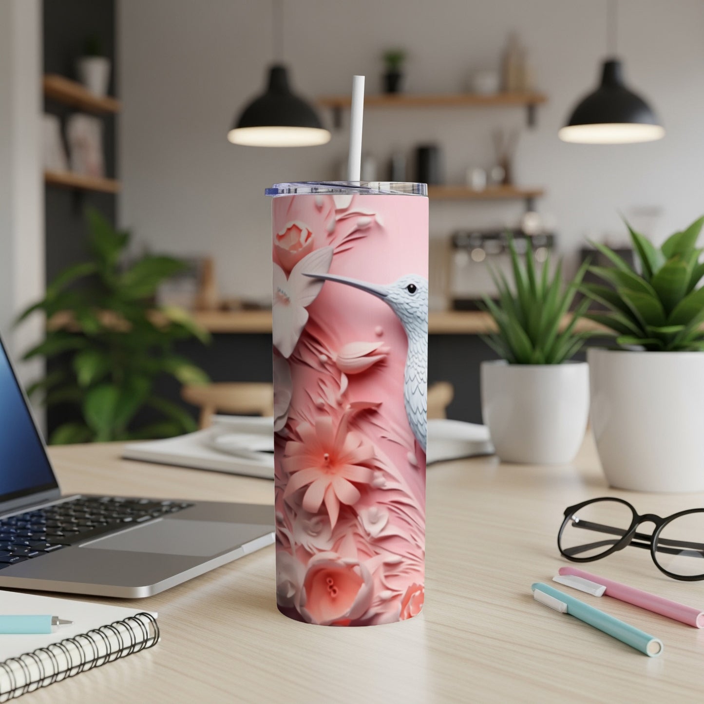 Pink hummingbird and floral patterned tumbler with a straw on a desk.
