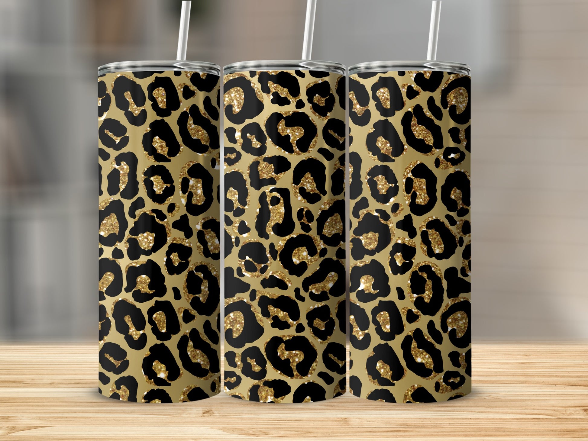 Three tumblers with leopard print design and gold glitter accents displayed on a wooden surface.