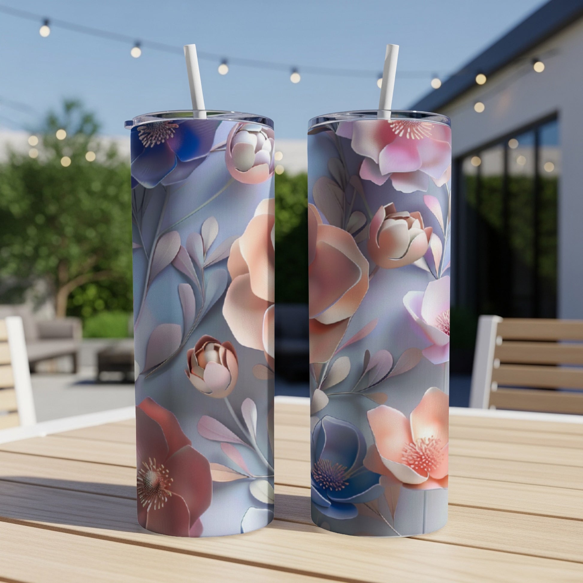 Two tall tumblers with floral patterns sit on a wooden table outdoors.