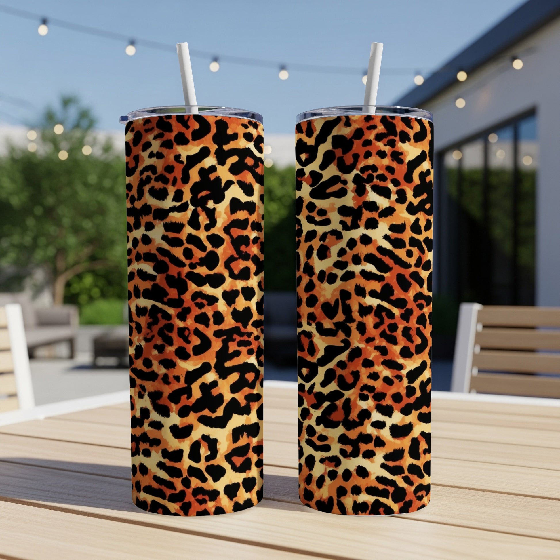 Two leopard print tumblers with straws on a table outdoors.