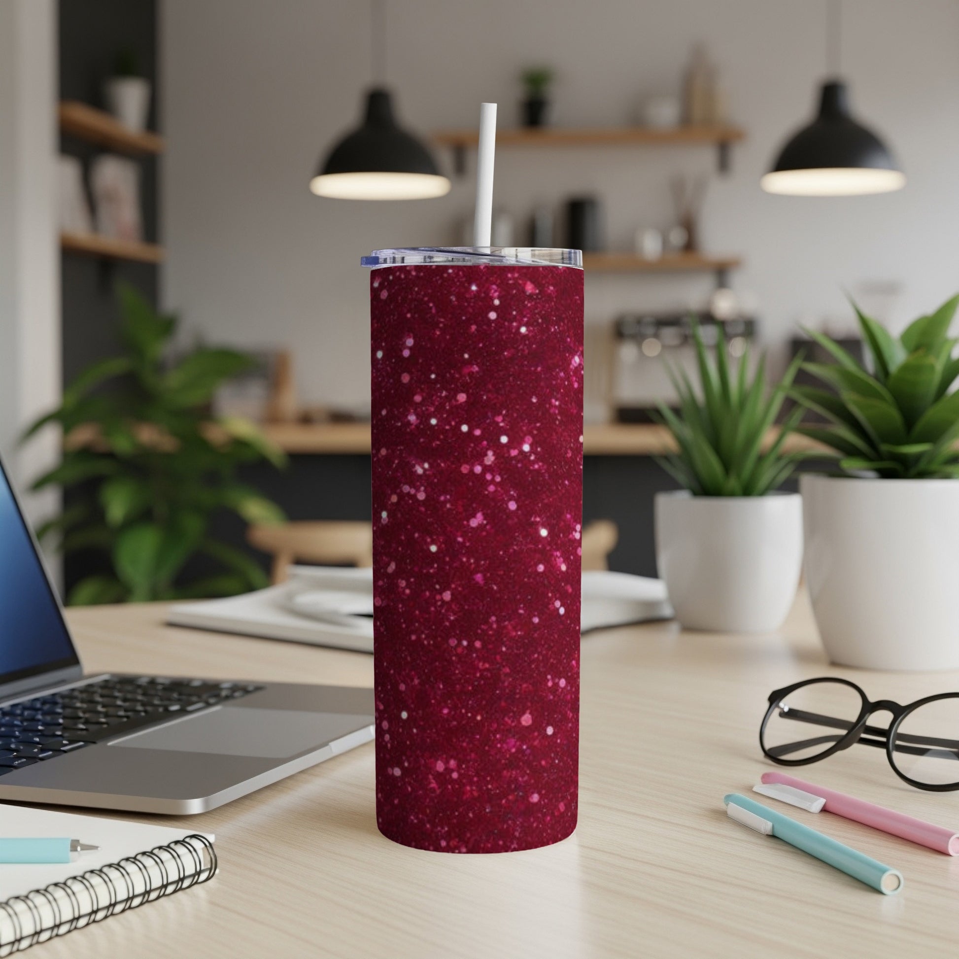 Glittering dark red skinny tumbler with a white straw on a desk.