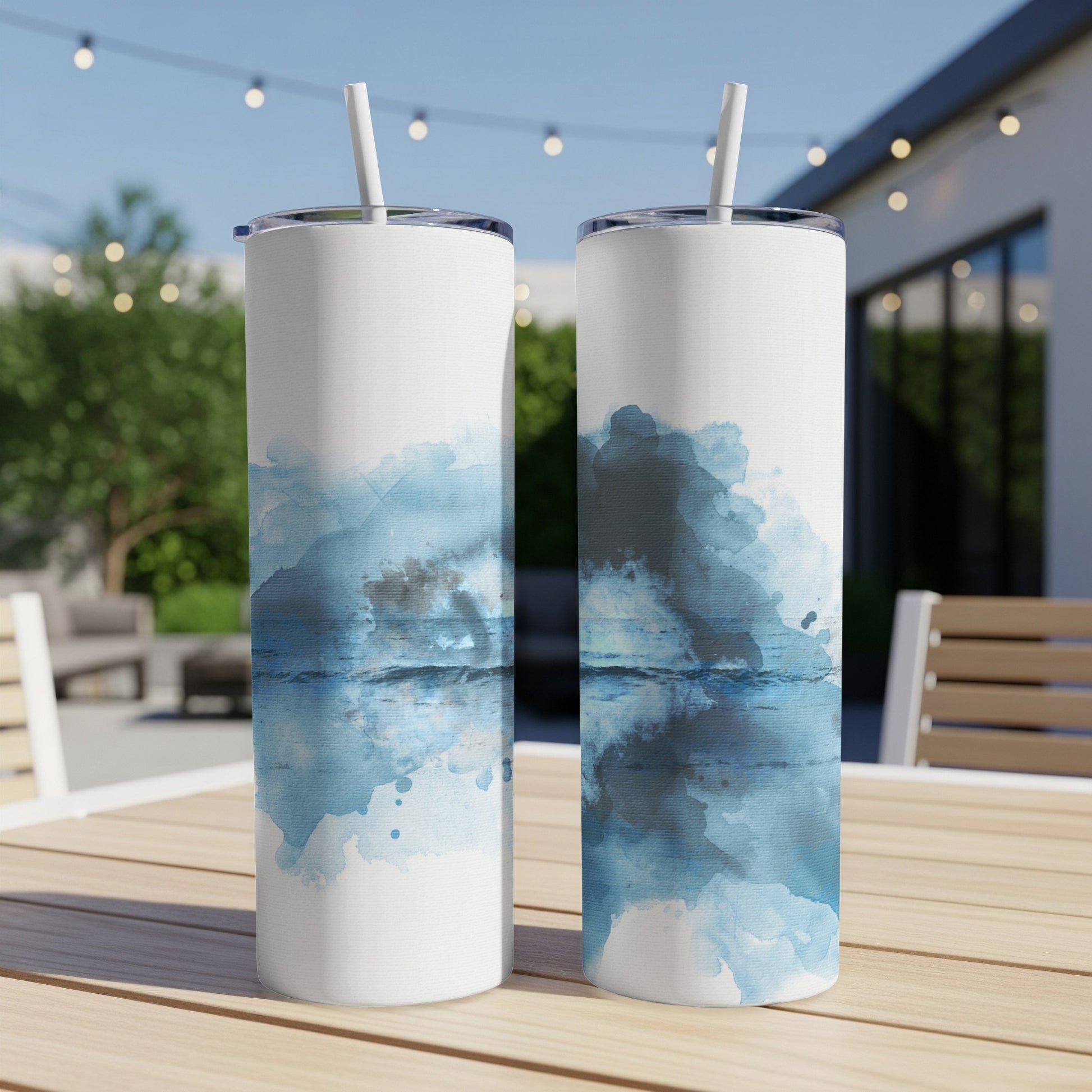 Two white tumblers with blue abstract watercolor design on a wooden table.