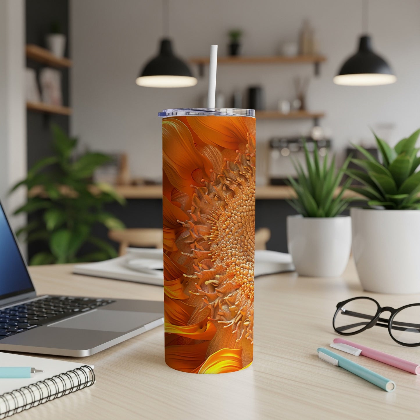 Orange sunflower tumbler with a straw on a desk next to a laptop.