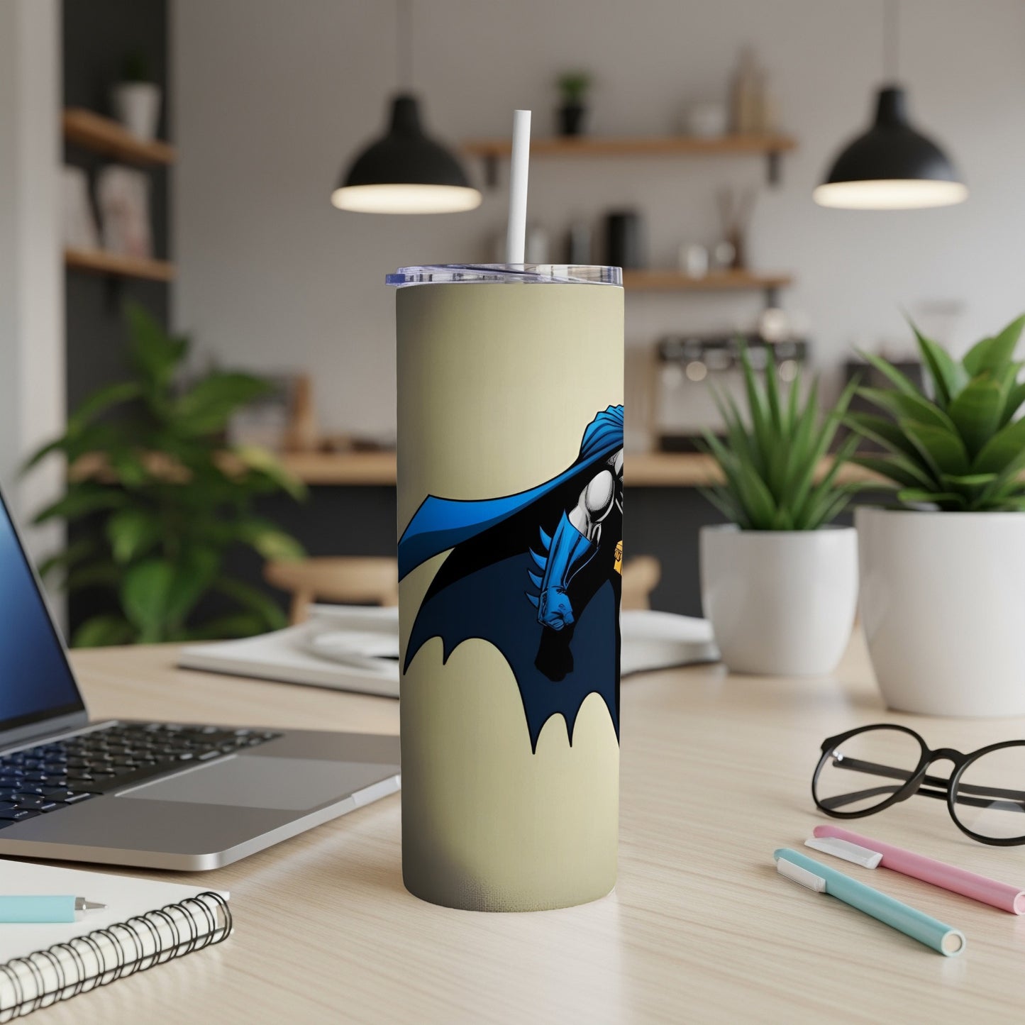 Batman tumbler with straw on a desk with laptop and eyeglasses.