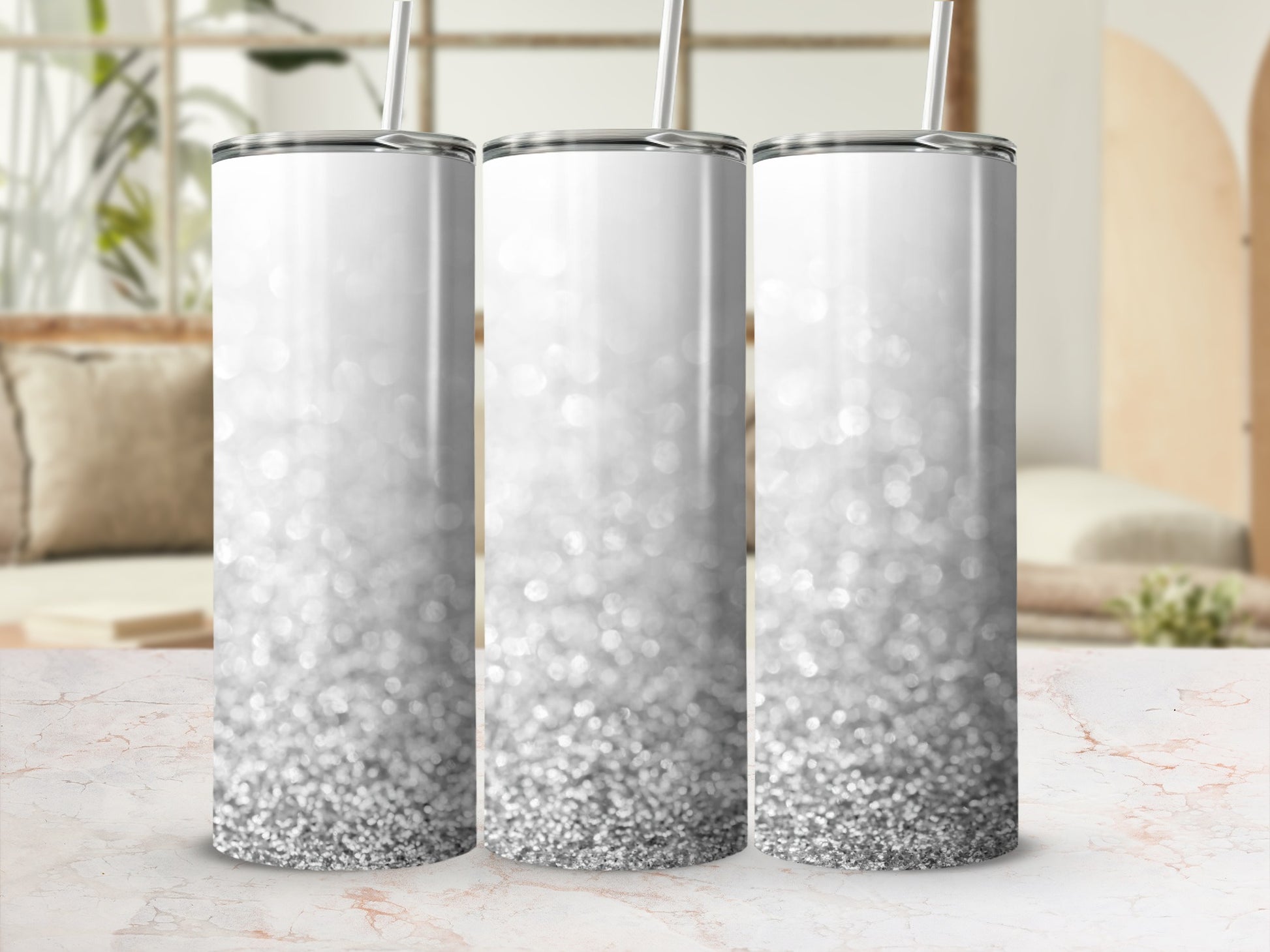 Three silver glitter tumblers with straws on a marble countertop.