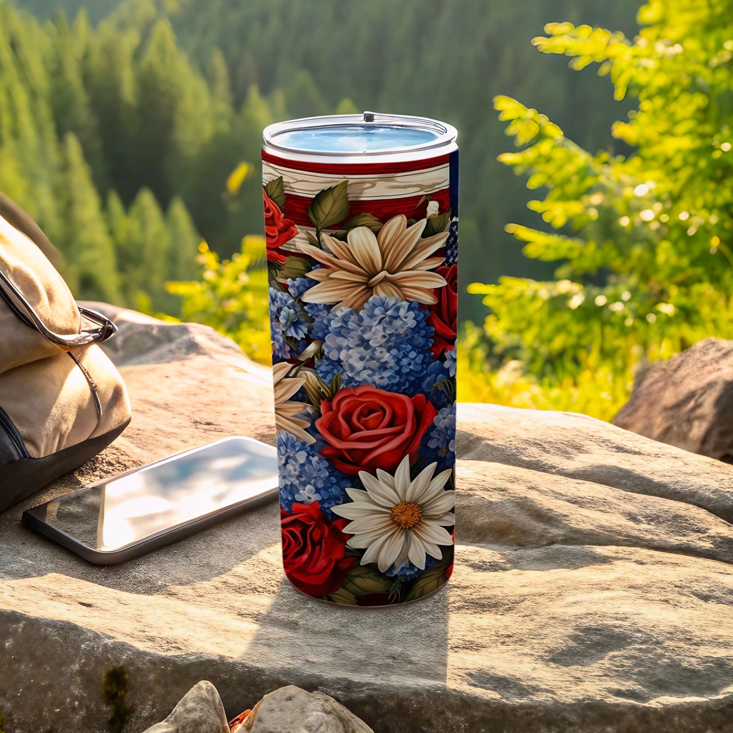 Tumbler with red roses, white daisies, and blue hydrangeas on rocky outcrop.