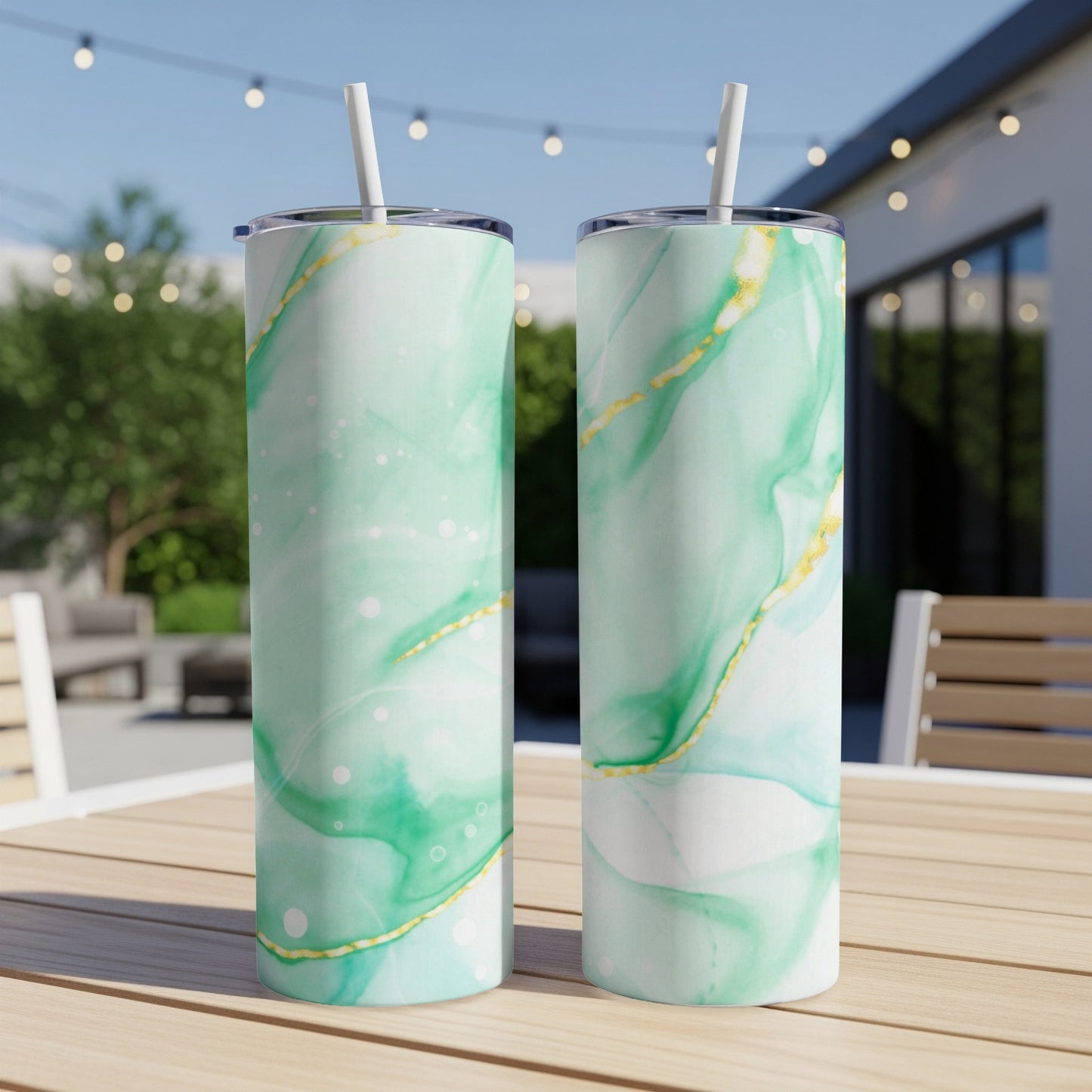 Two green and gold marbled tumblers with straws on a wooden table outdoors.
