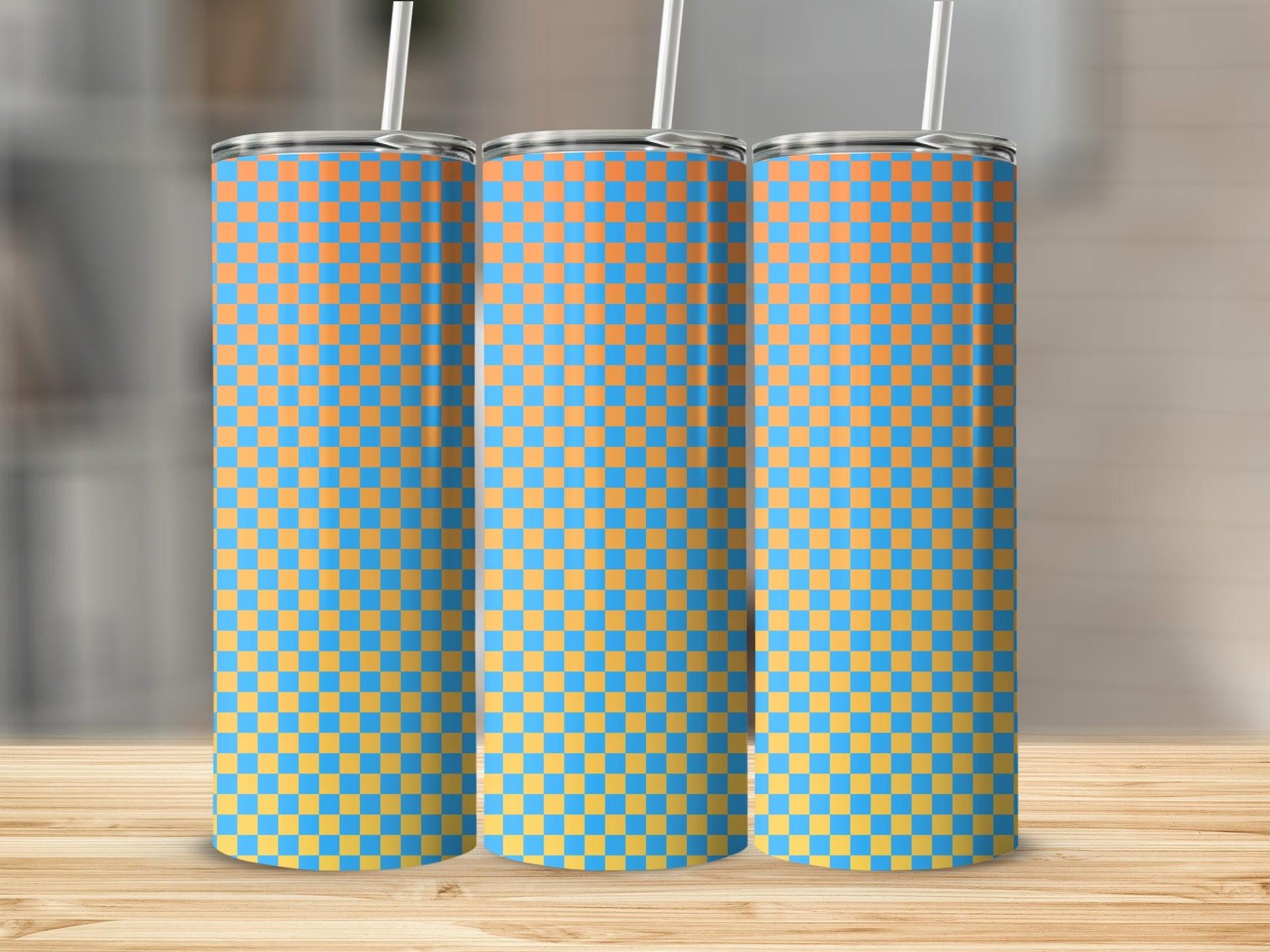 Three blue and orange checkered tumblers with straws on a wooden surface.