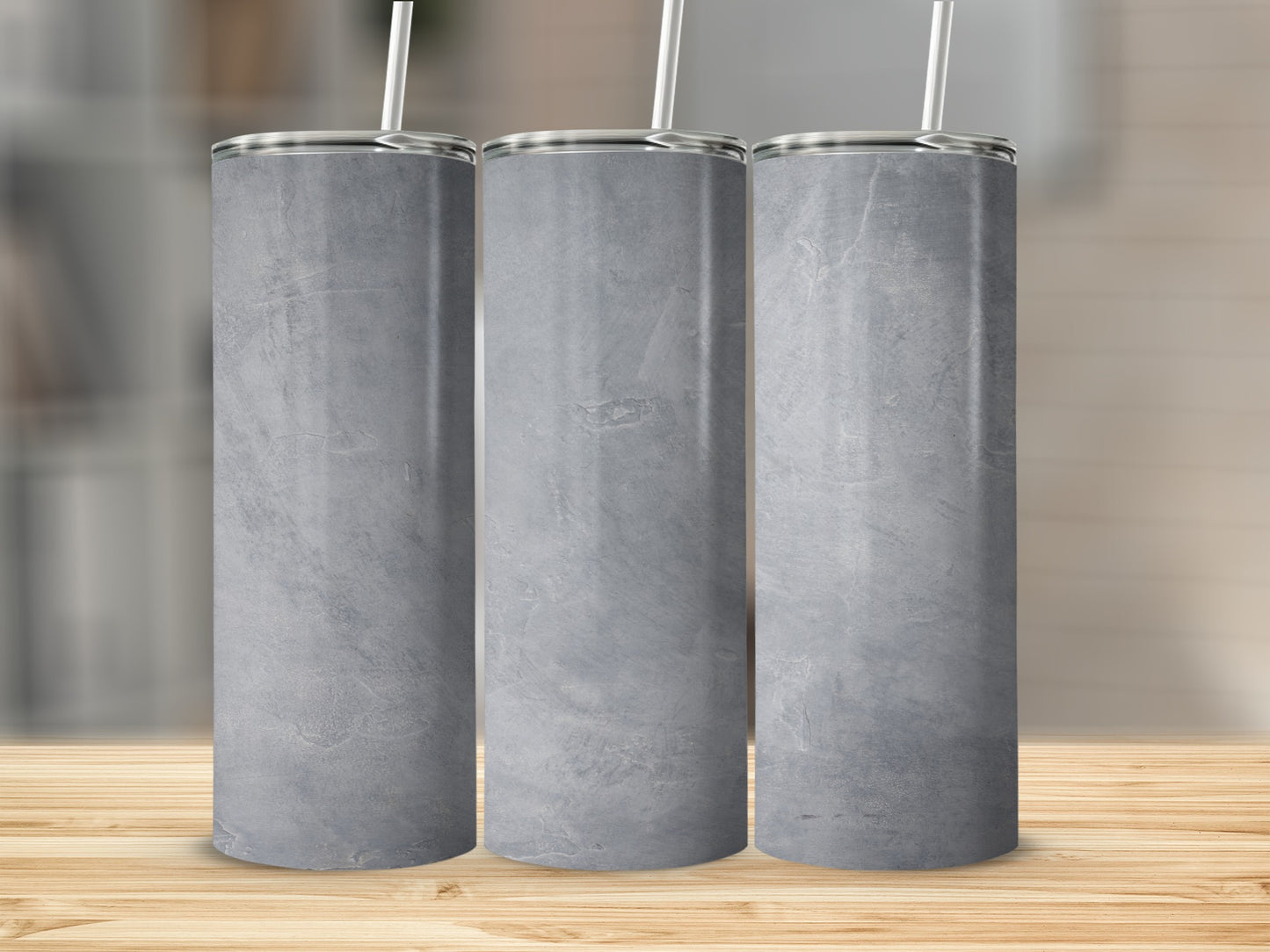 Three gray marbled tumblers with straws on a wooden surface.