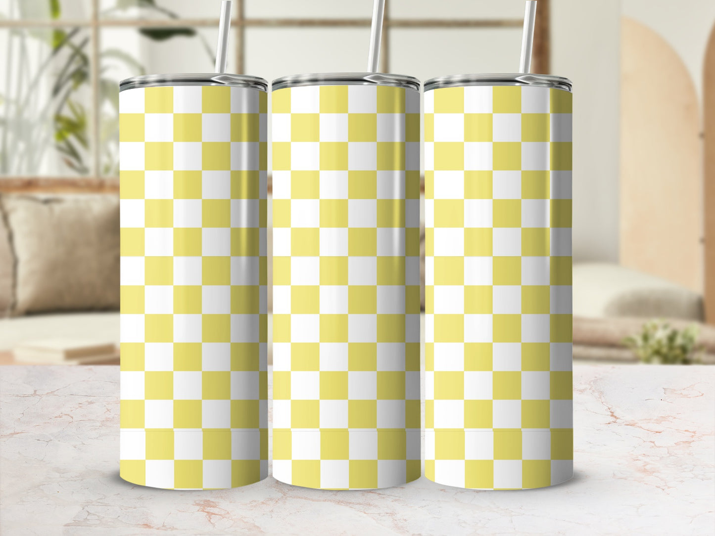 Three yellow and white checkered tumblers with straws on a marble surface.